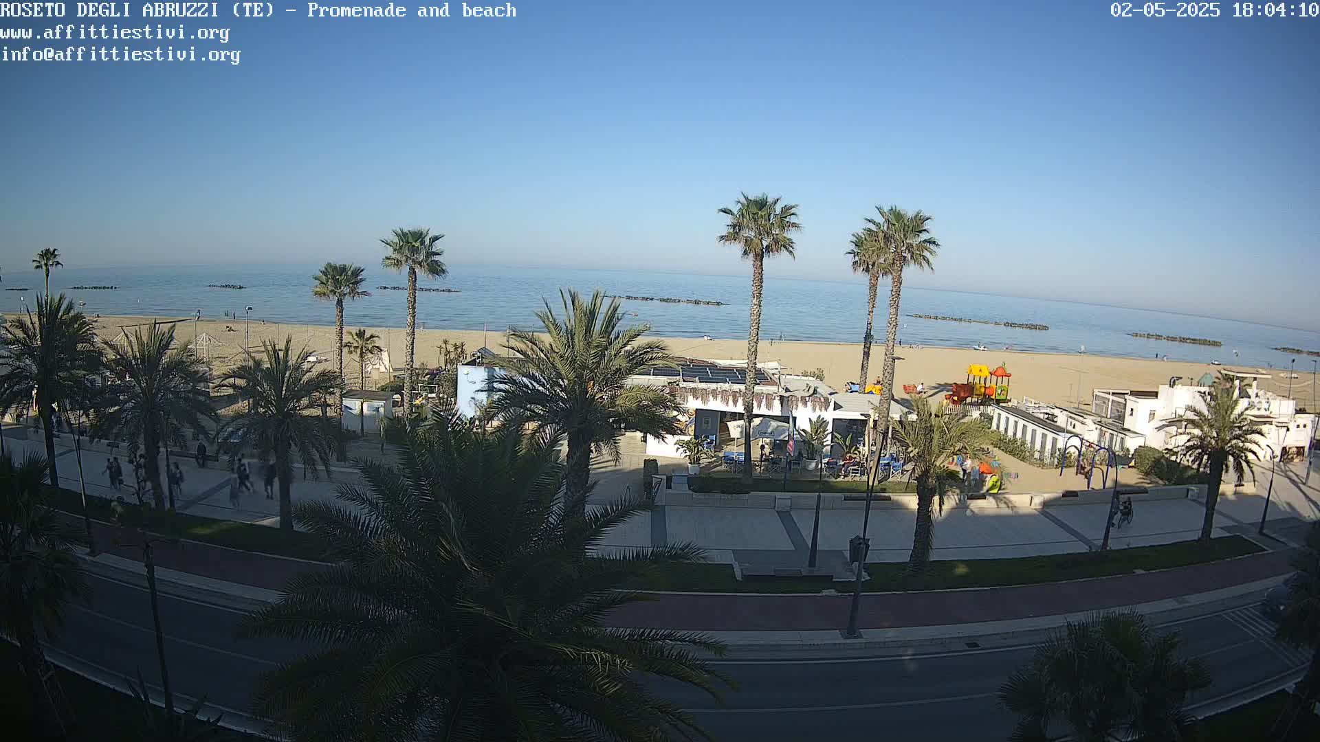 A beach with palm trees, a promenade, and a playground is visible under a clear blue sky.