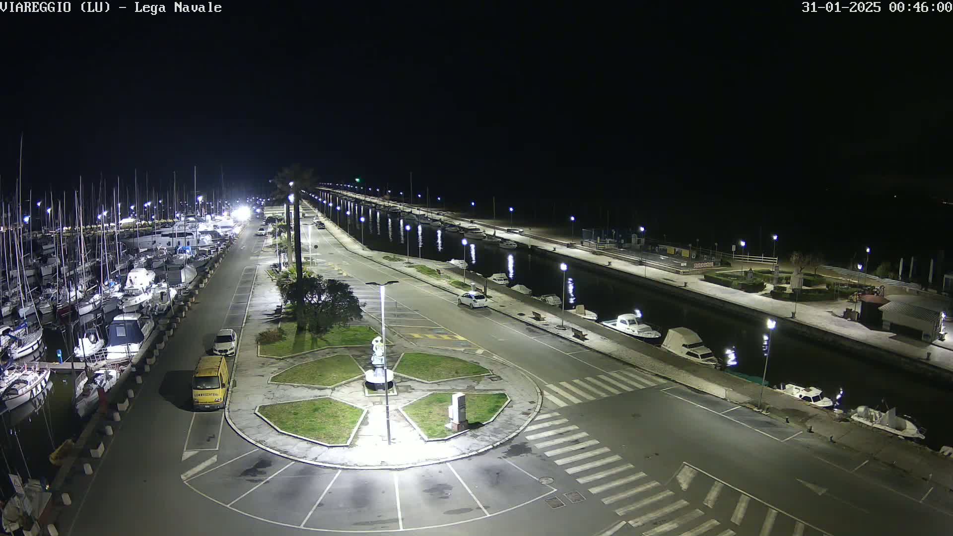 A nighttime aerial view of a marina with numerous boats docked along a canal, surrounded by empty parking lots and streetlights.