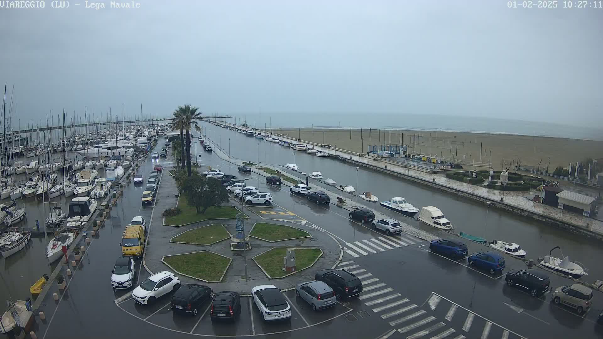A marina with many boats is partially flooded, with rain-slicked streets and cars parked around a central plaza.