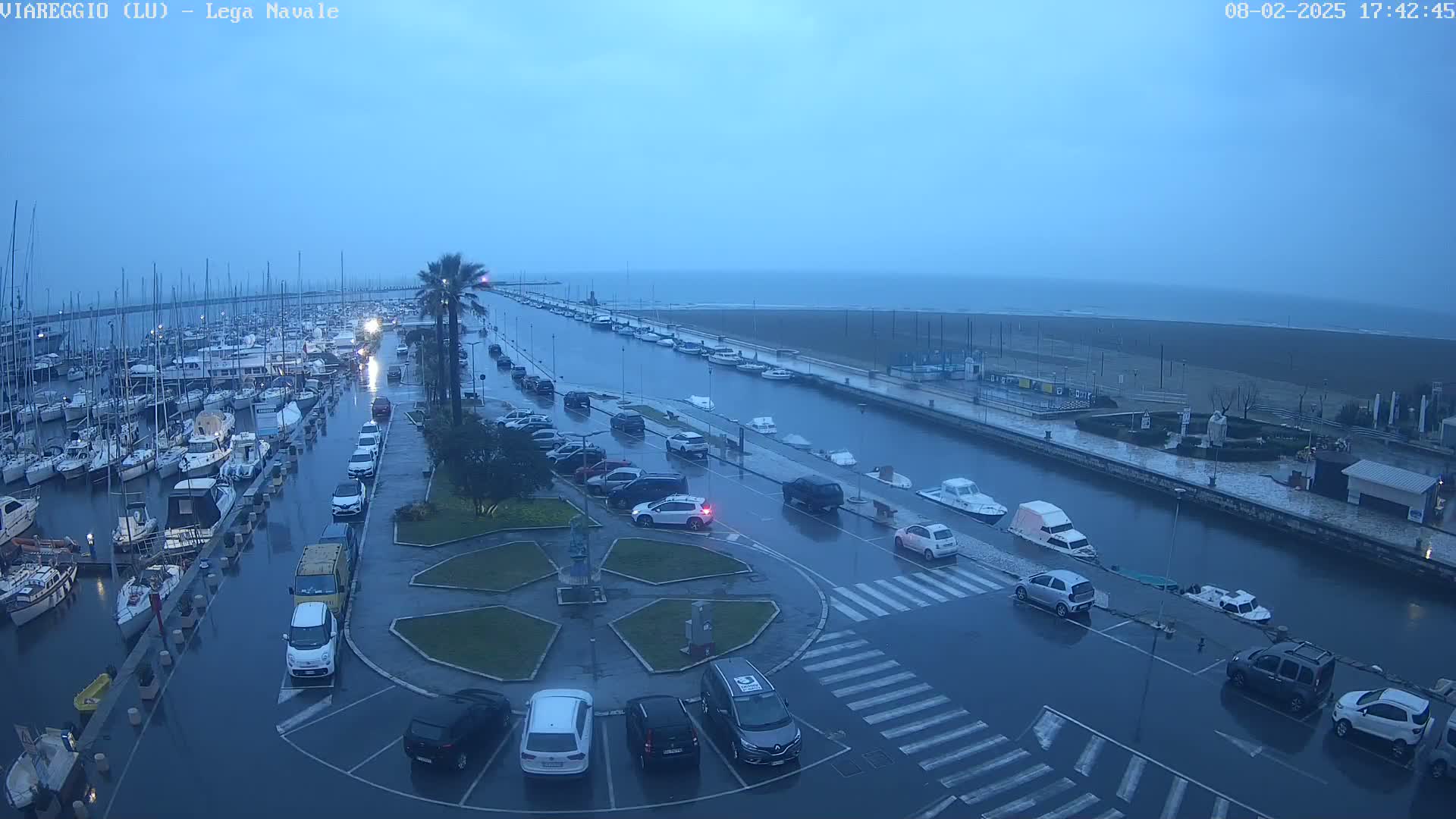 A marina and surrounding area are flooded under a gray, overcast sky, with cars parked in the water and along the streets.