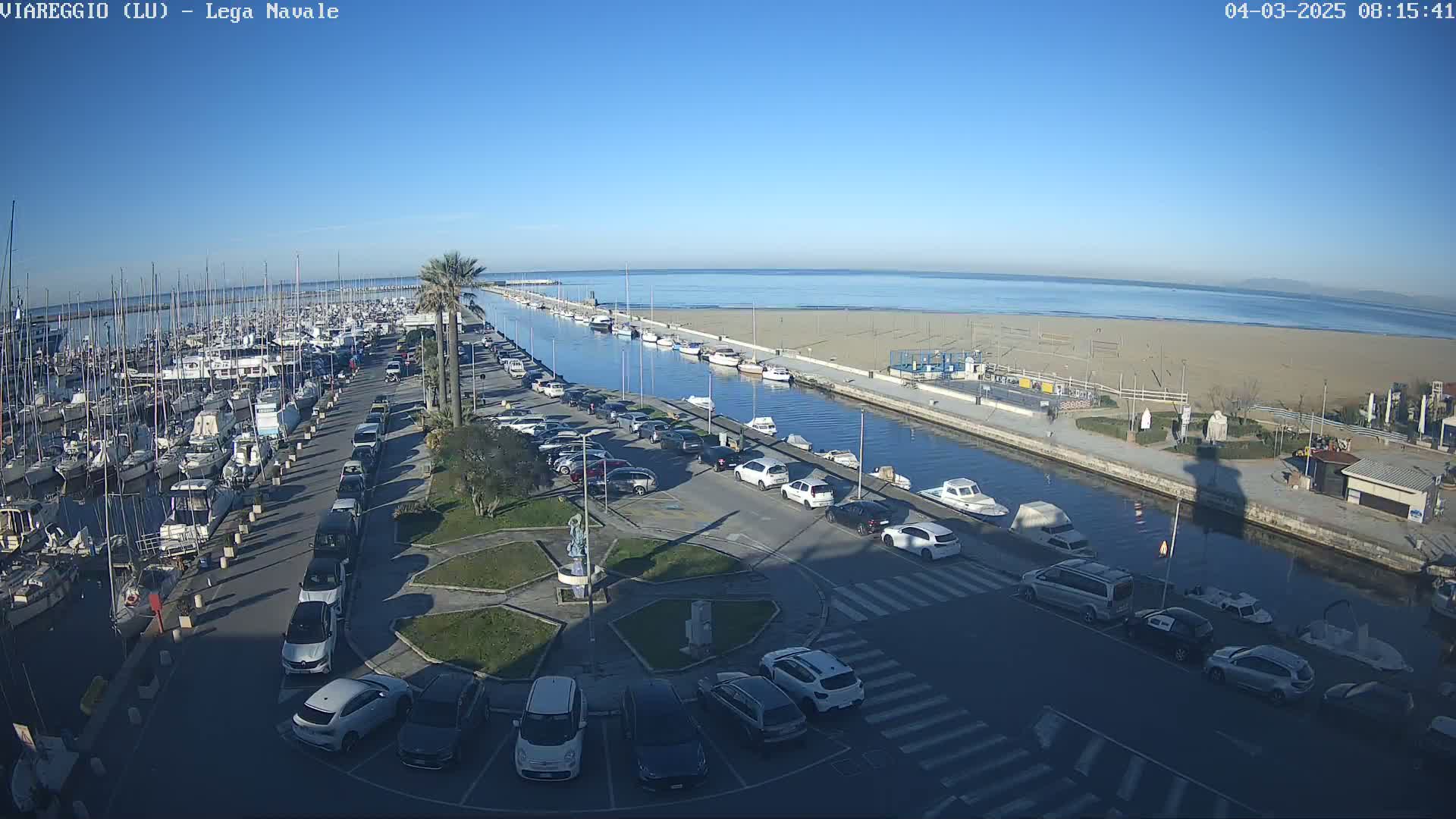 A harbor filled with boats is next to a sandy beach on a sunny day.