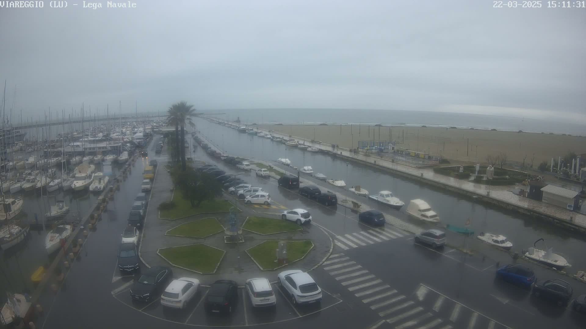A rain-soaked marina and waterfront area with numerous parked cars and boats, under an overcast sky.
