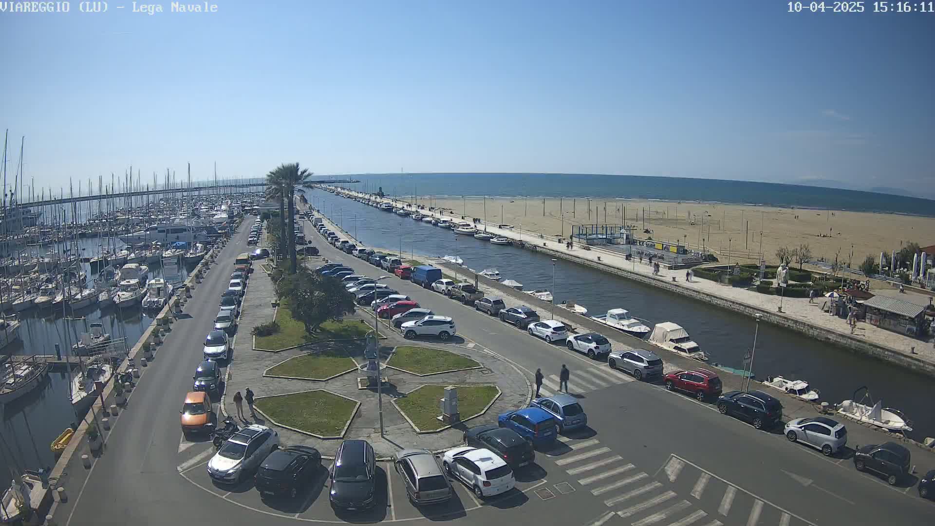 A marina filled with boats, next to a canal and sandy beach, on a sunny day.