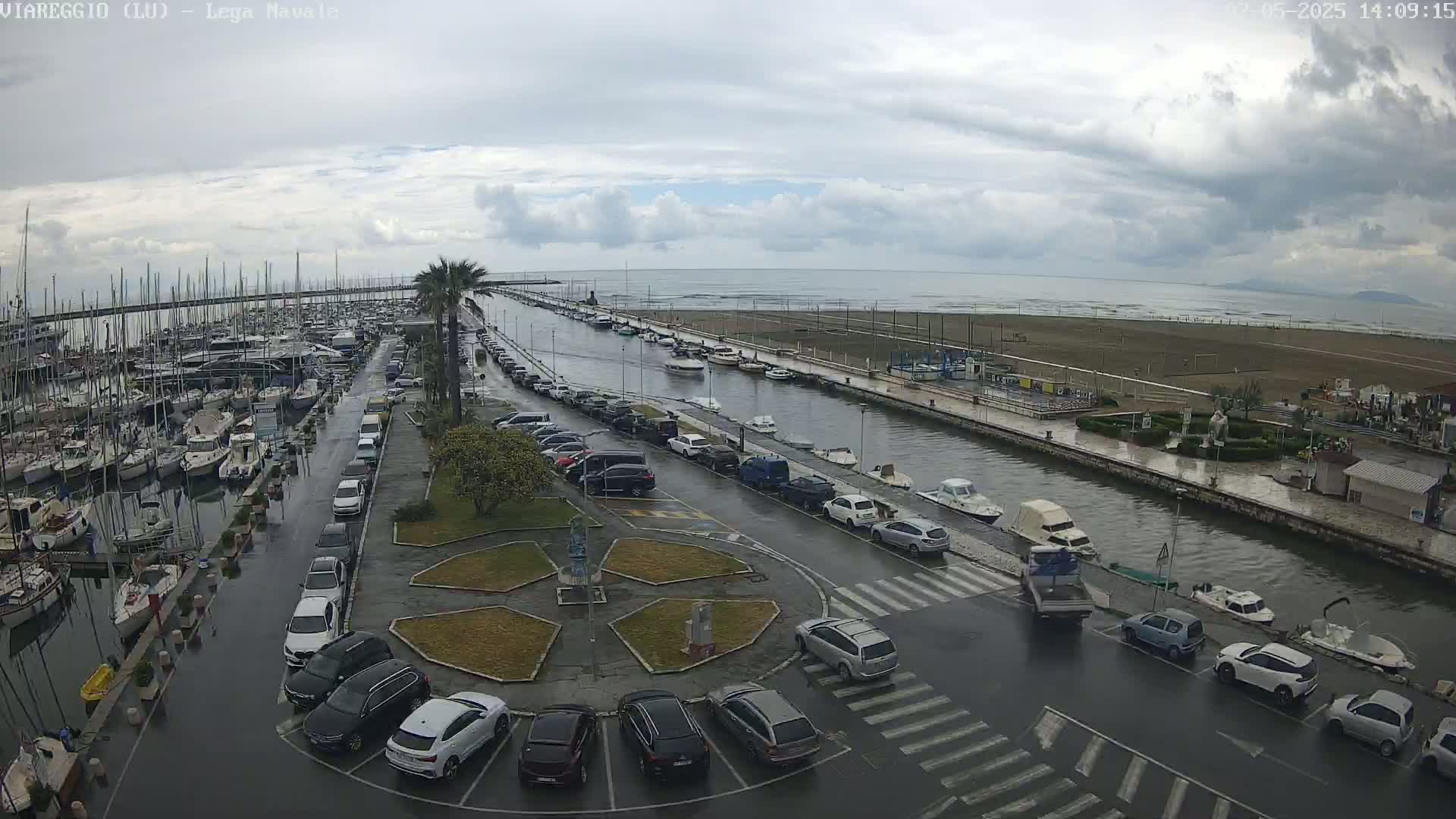 A wet marina filled with boats and cars is shown on an overcast day next to a calm sea.