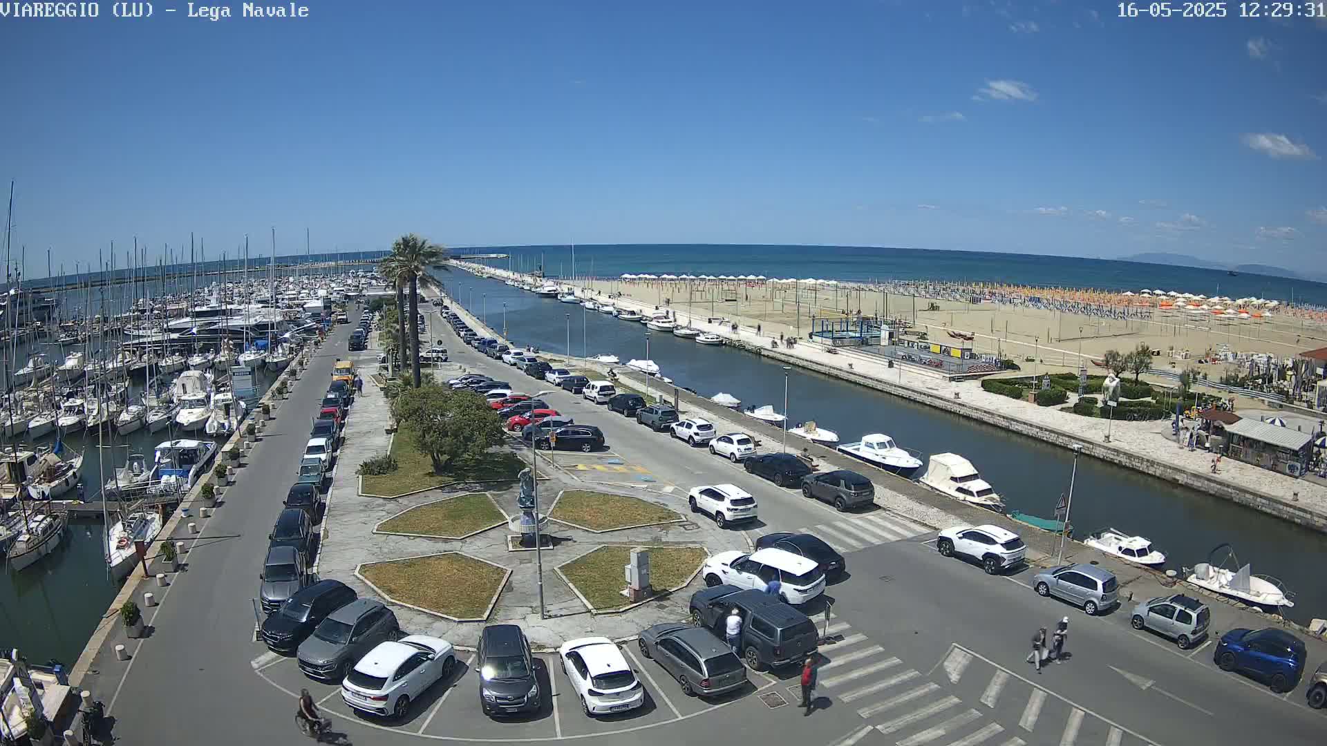 A marina filled with boats is adjacent to a canal and beach on a sunny day.