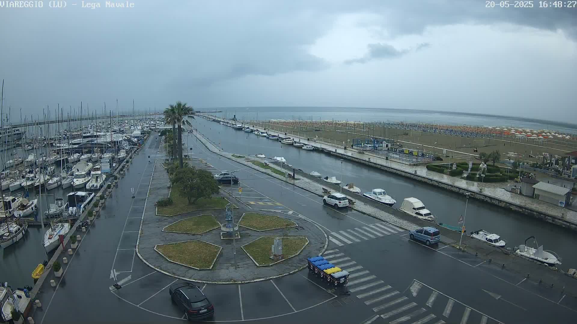 A wet marina filled with boats is next to a canal and beach under a cloudy sky.