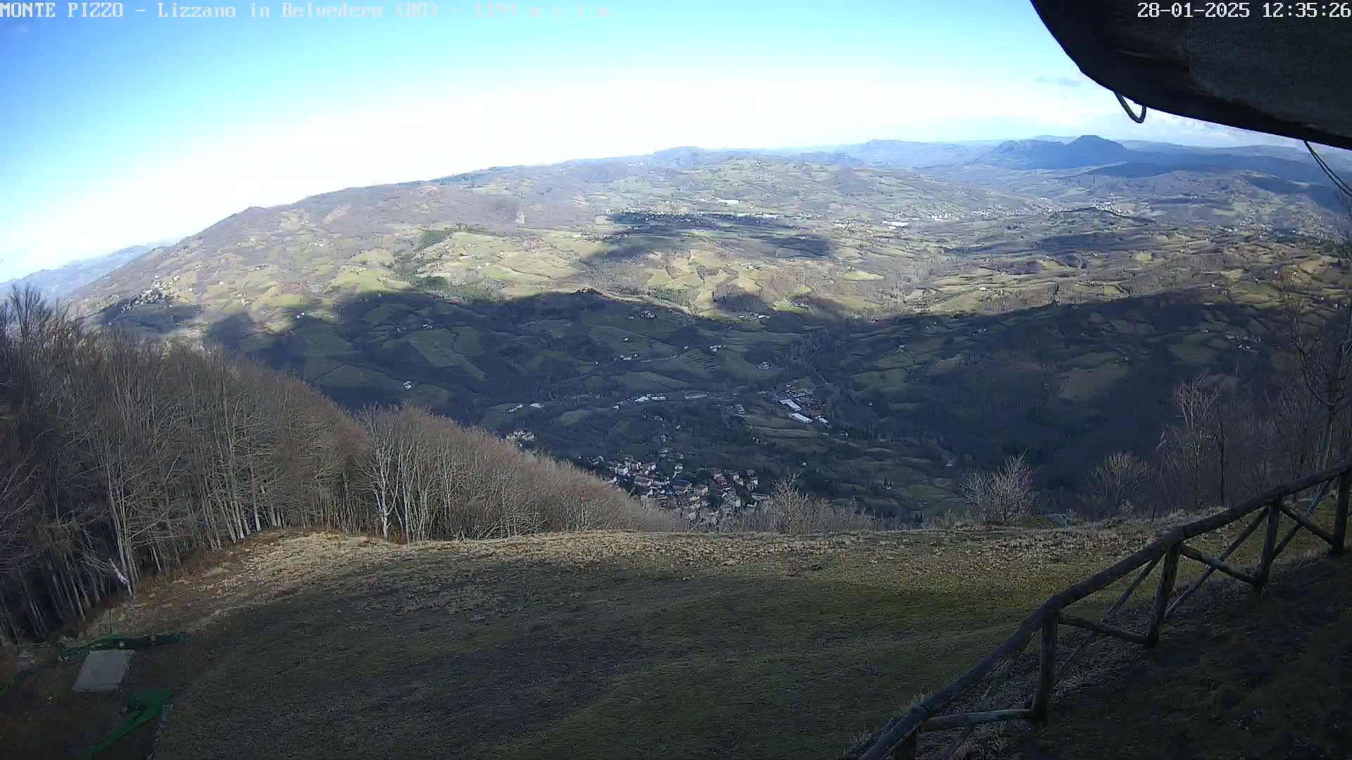 A high-angle, long shot on a sunny day shows a sprawling valley of farmland and small villages nestled among rolling hills and forests.