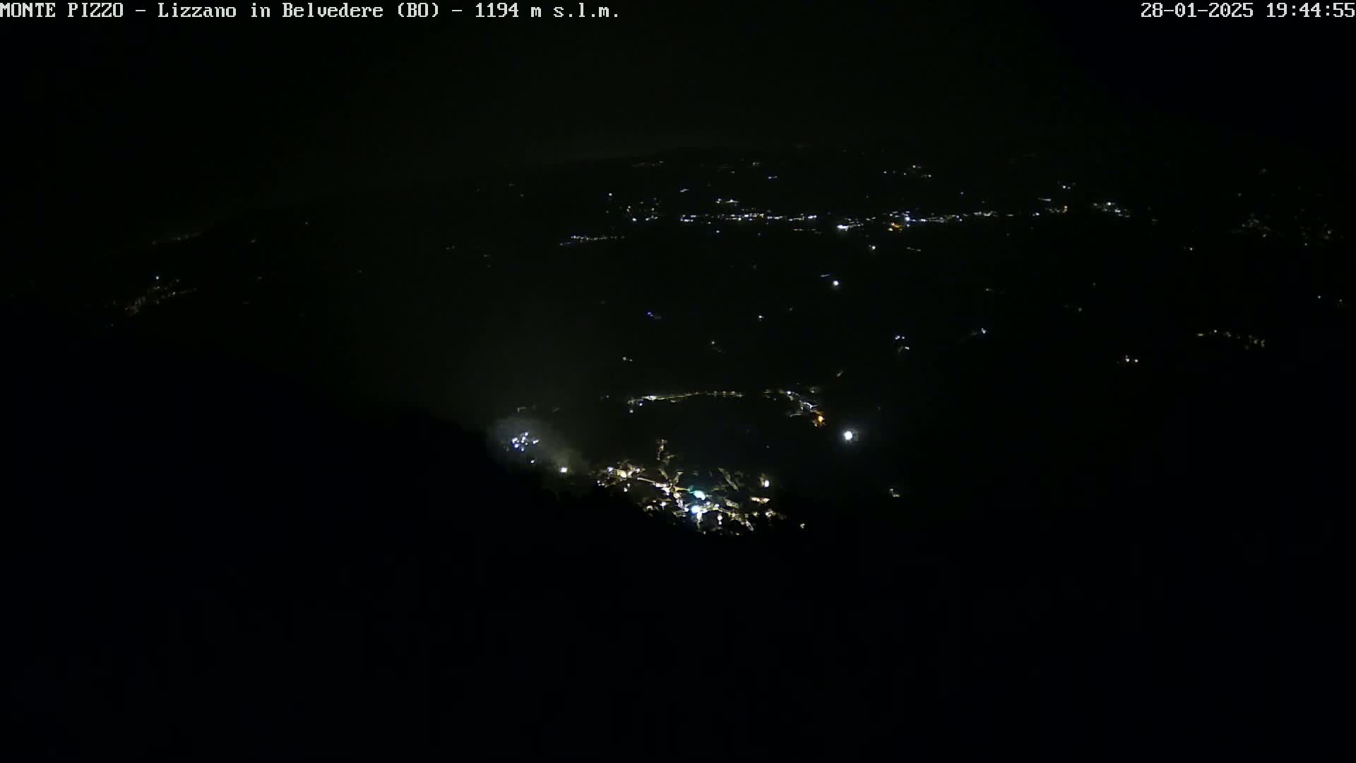 A nighttime, high-angle view shows a scattering of lights from a town or village nestled in a dark landscape.