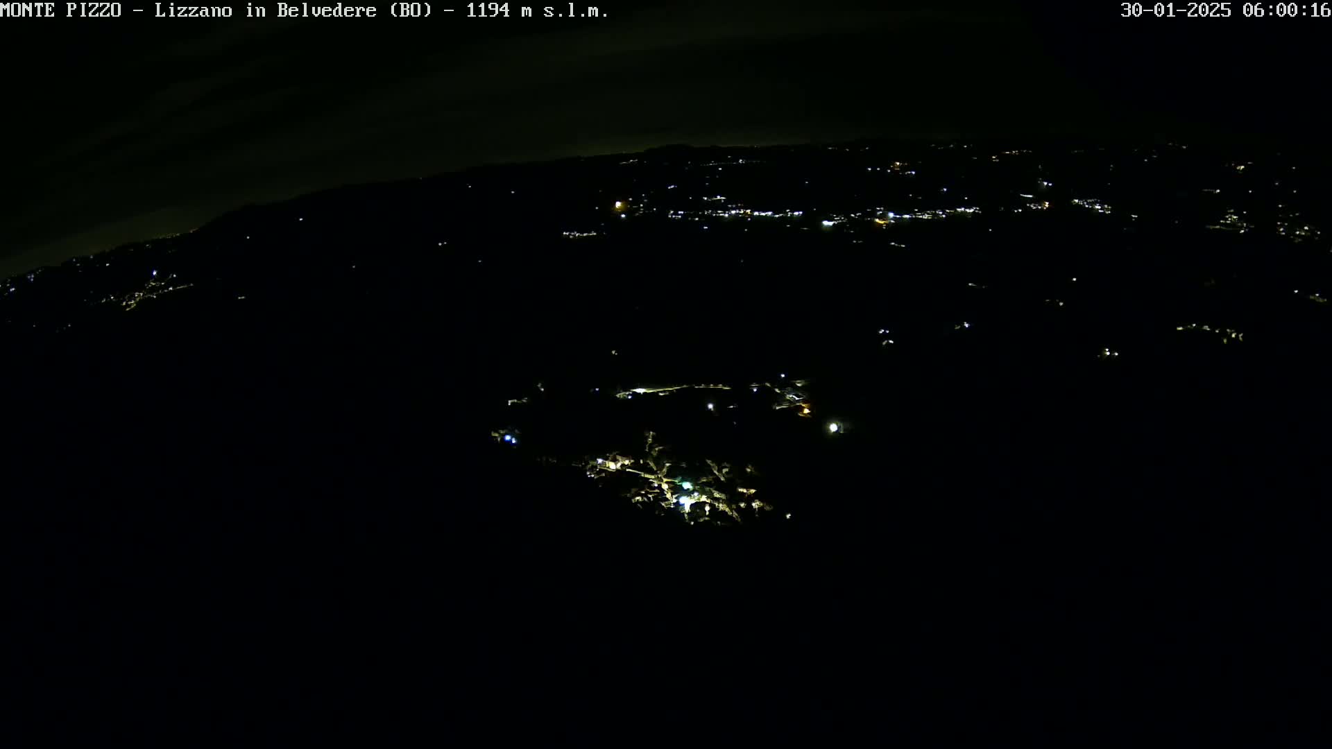 A nighttime aerial view shows a dark landscape with sparsely scattered lights from a town below.