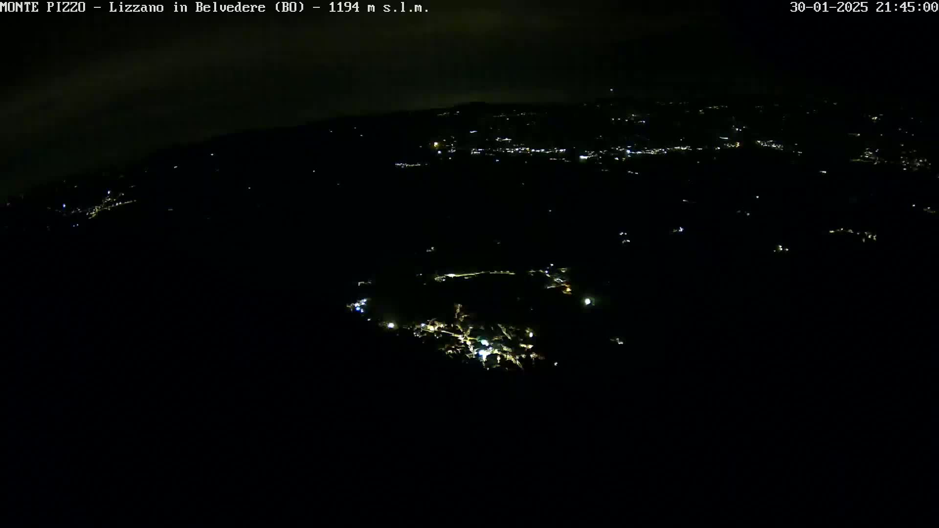 A nighttime, high-angle view shows a cluster of dimly lit buildings and houses scattered across a dark landscape.