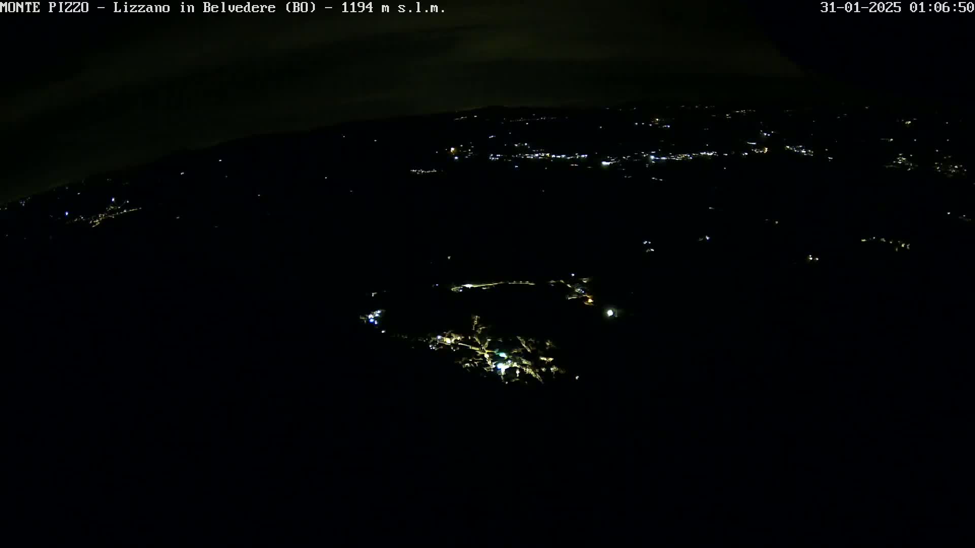 A nighttime, aerial view shows a sparsely lit town nestled in a dark landscape under a mostly clear sky.