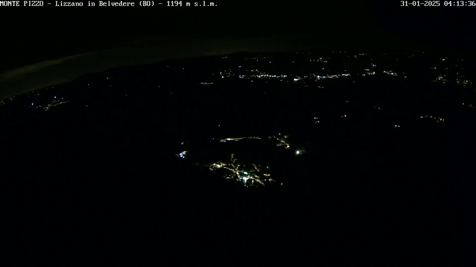 A nighttime, high-angle view shows a sparsely lit landscape with scattered points of light from a town below.