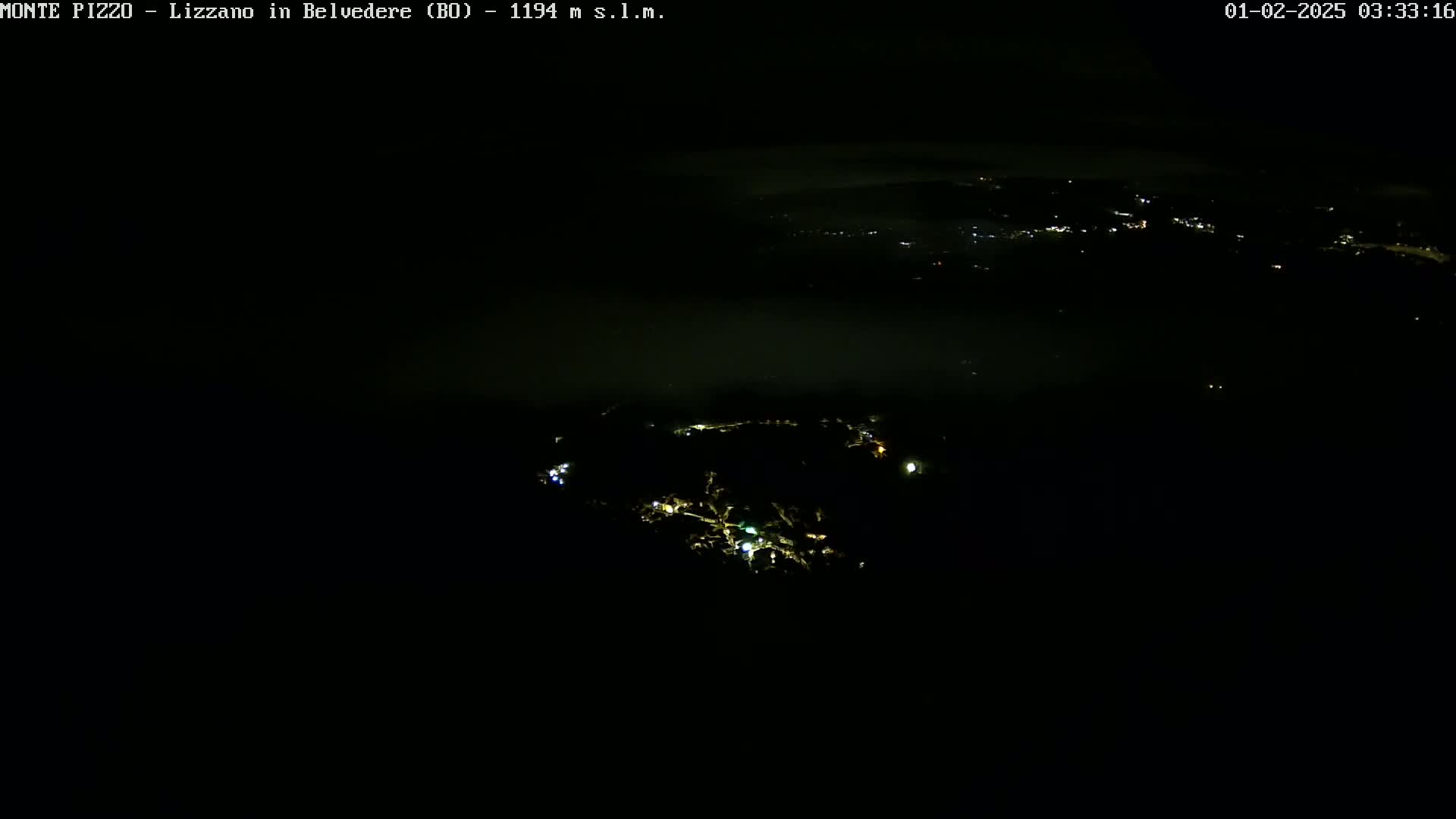 A nighttime aerial view shows a town's scattered lights partially obscured by low-lying fog or clouds.