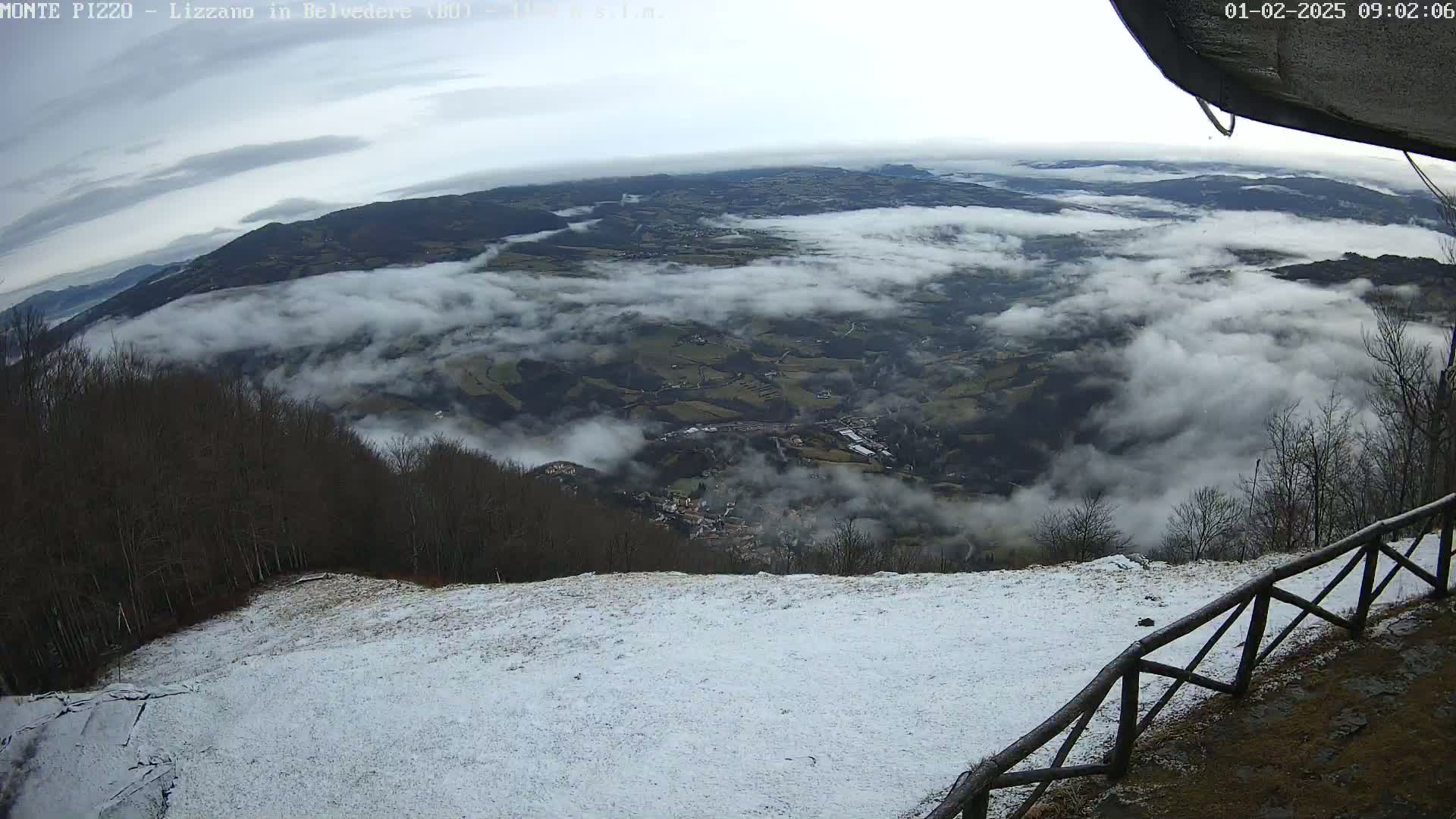 A snow-covered hillside overlooks a valley shrouded in low-lying clouds under an overcast sky.