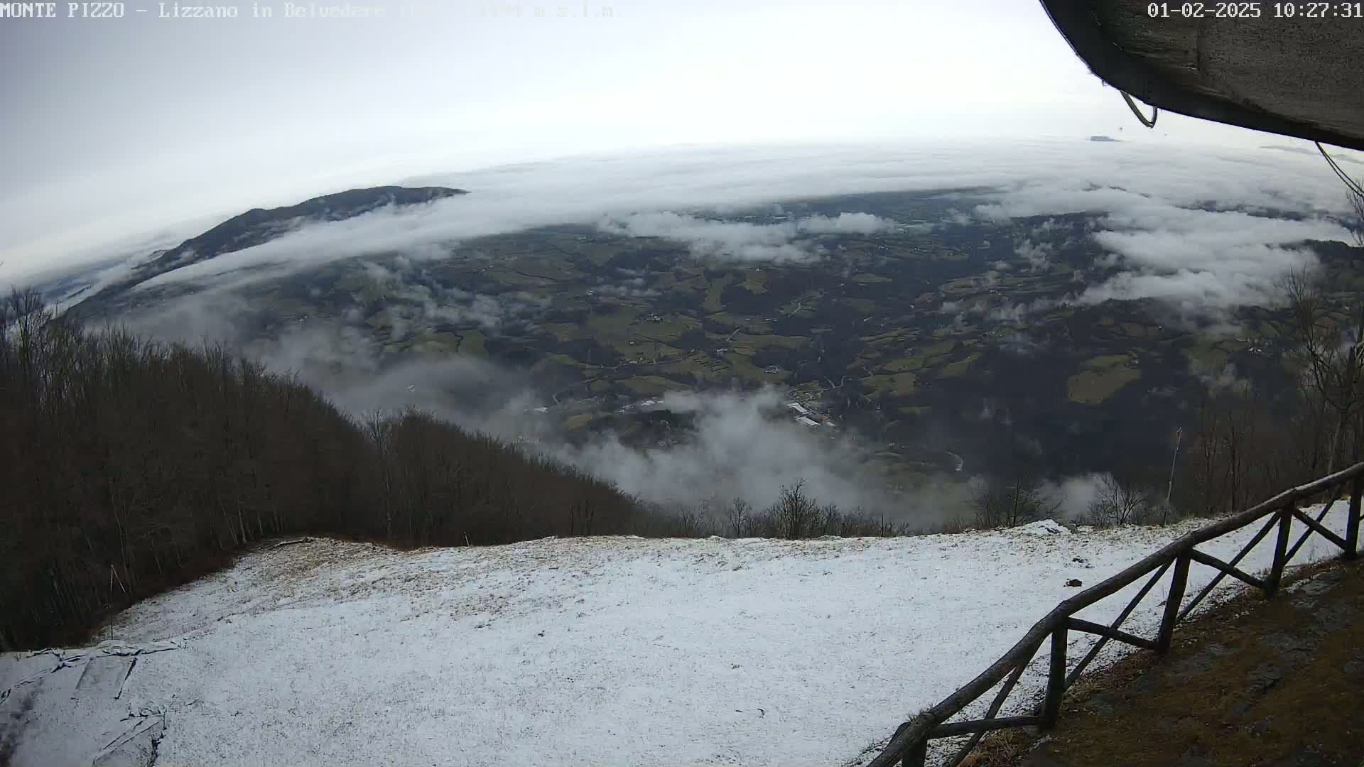 A snow-covered hillside overlooks a valley shrouded in fog and clouds.