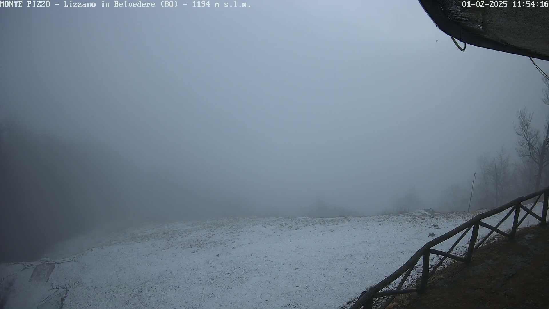 A snow-covered landscape is shrouded in thick fog, with a wooden fence visible in the foreground.