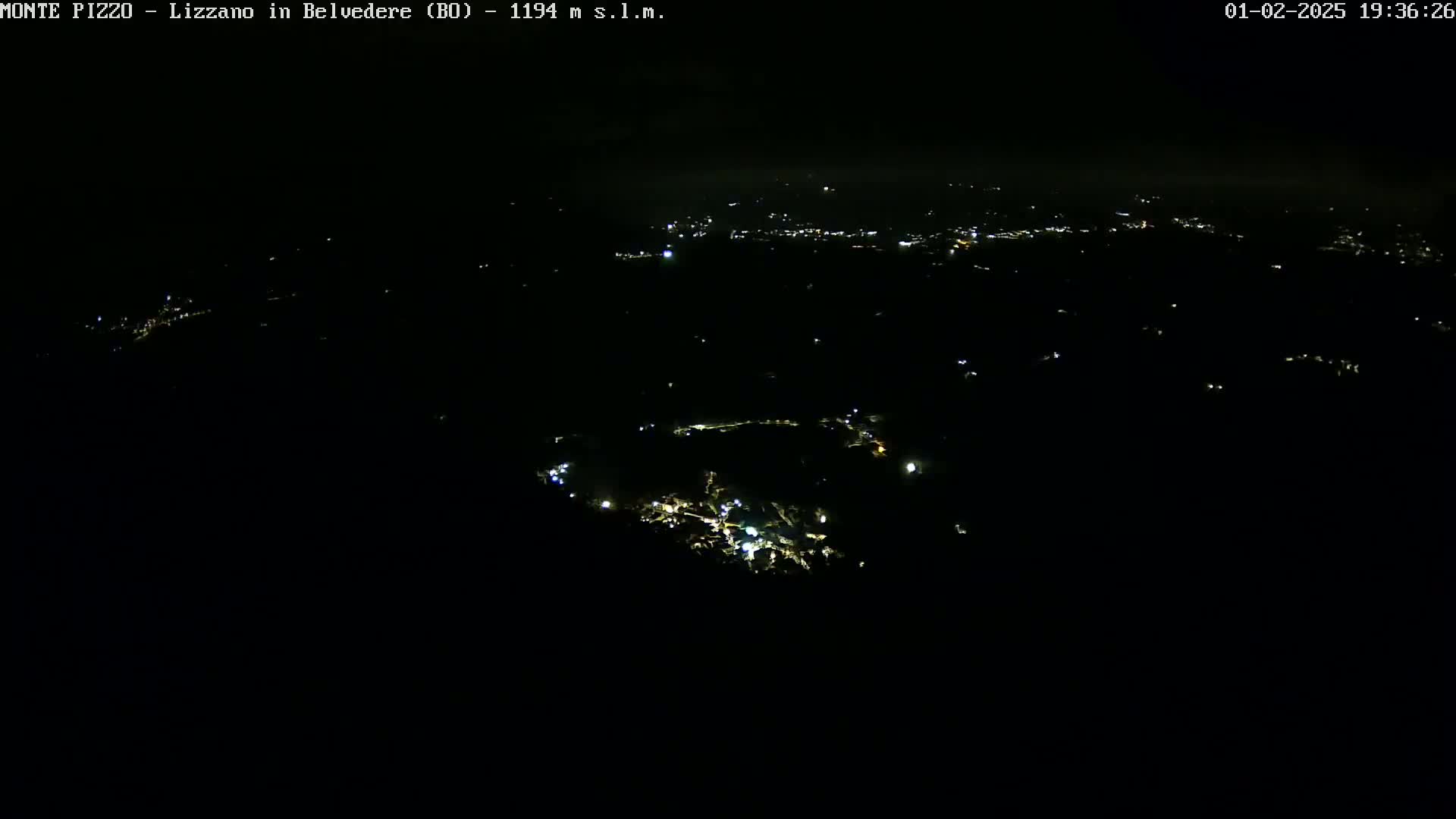 A nighttime, high-angle view of sparsely lit settlements nestled in a dark, possibly mountainous landscape under a clear sky.