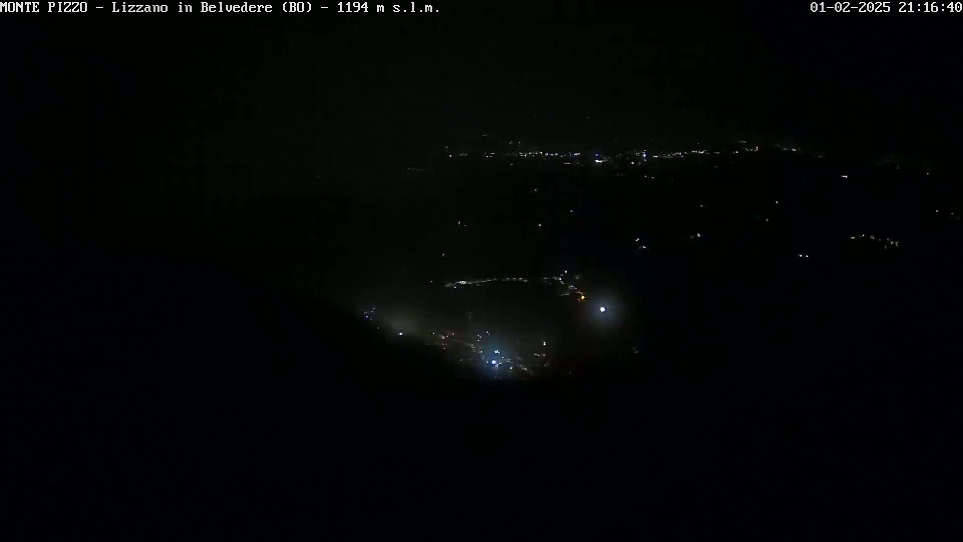 A nighttime, high-angle view shows a scattering of faint lights across a dark landscape.