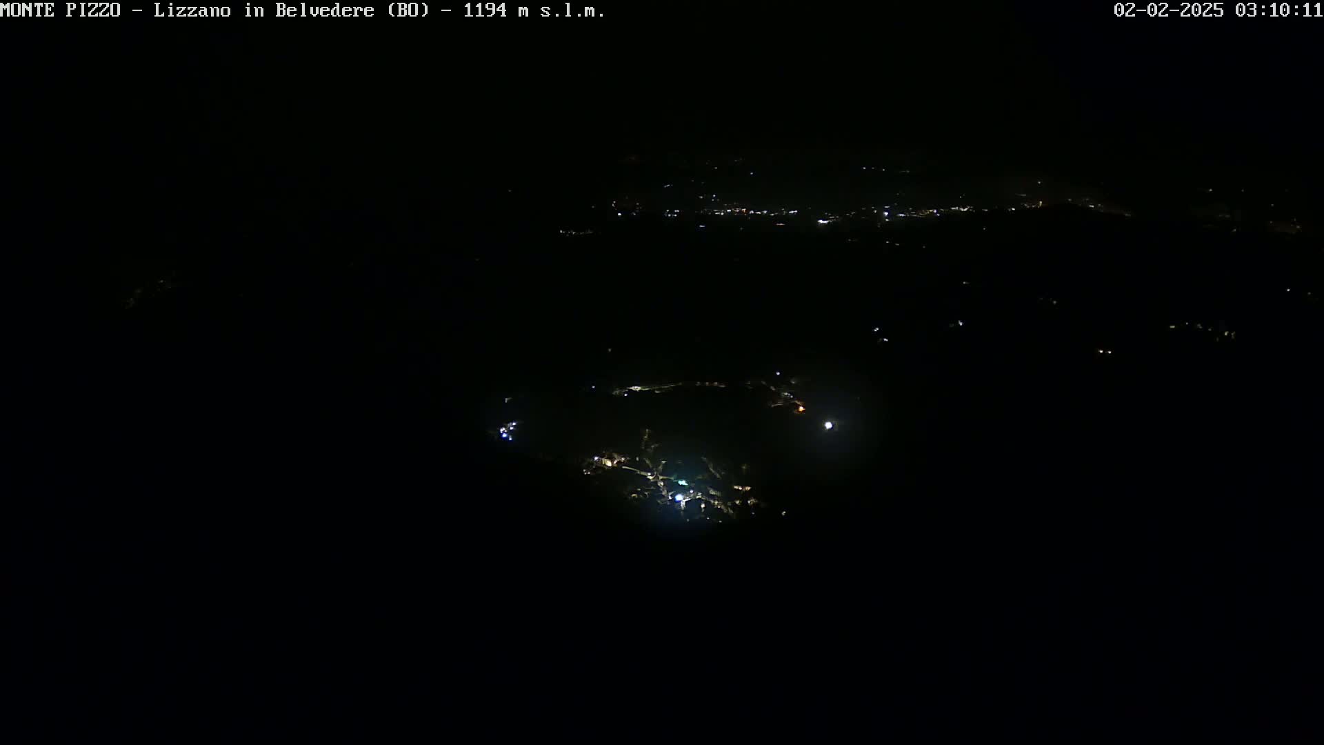 A nighttime, high-angle view shows a sparsely lit landscape with a few scattered lights visible in the darkness.