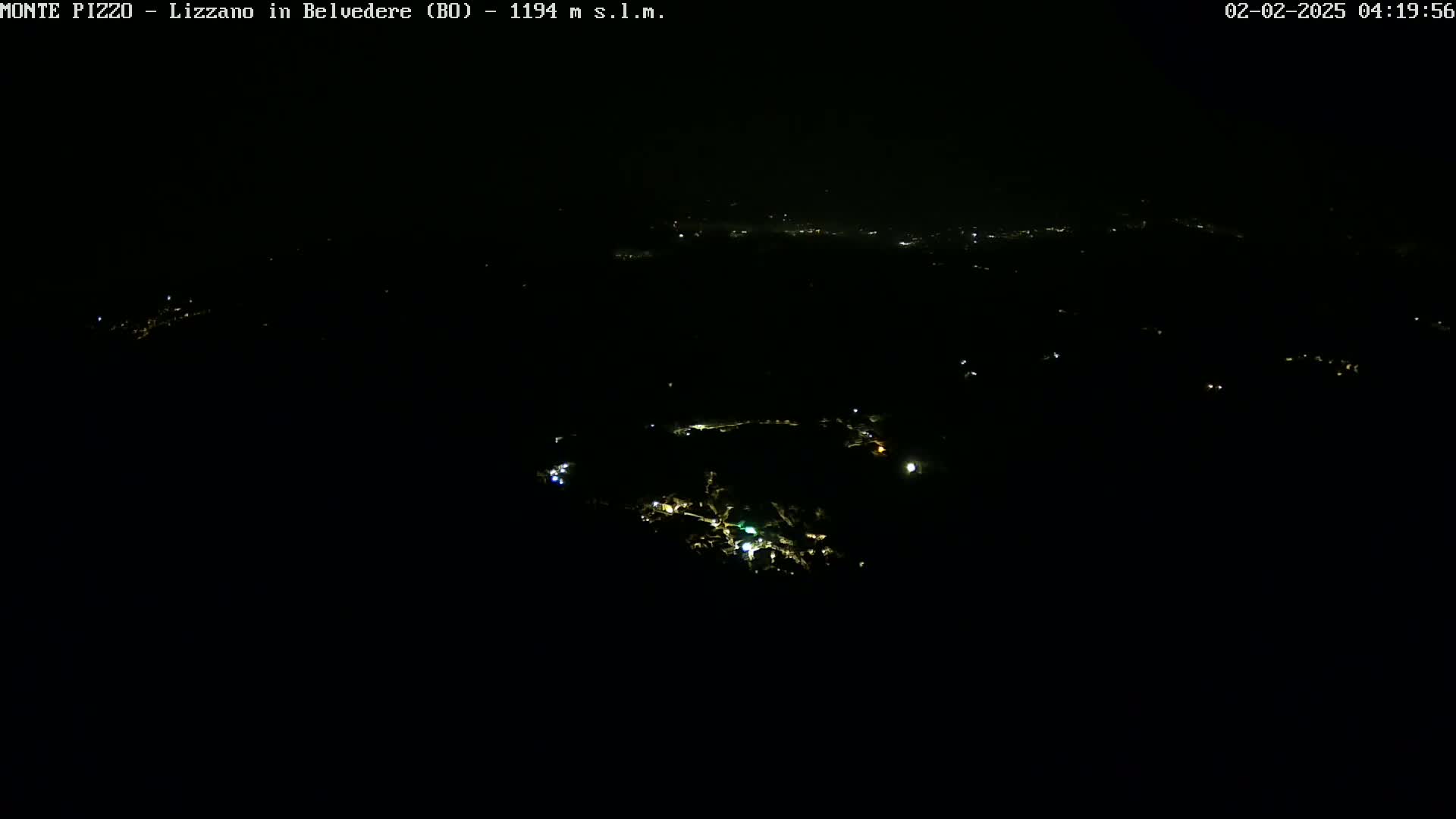 A nighttime, high-angle view shows a small town with scattered lights against a completely dark sky.