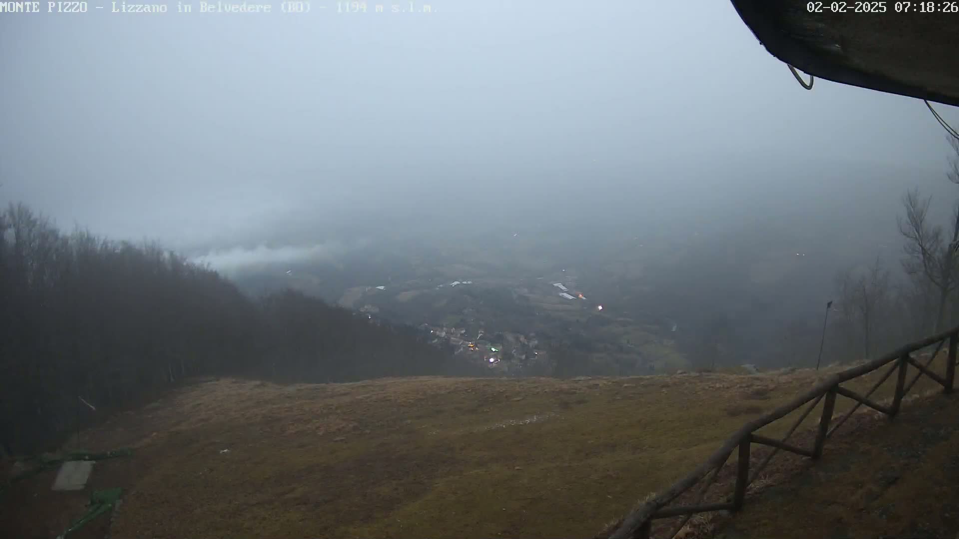 A foggy, overcast view from a mountaintop shows a valley with a small town below, partially obscured by mist.
