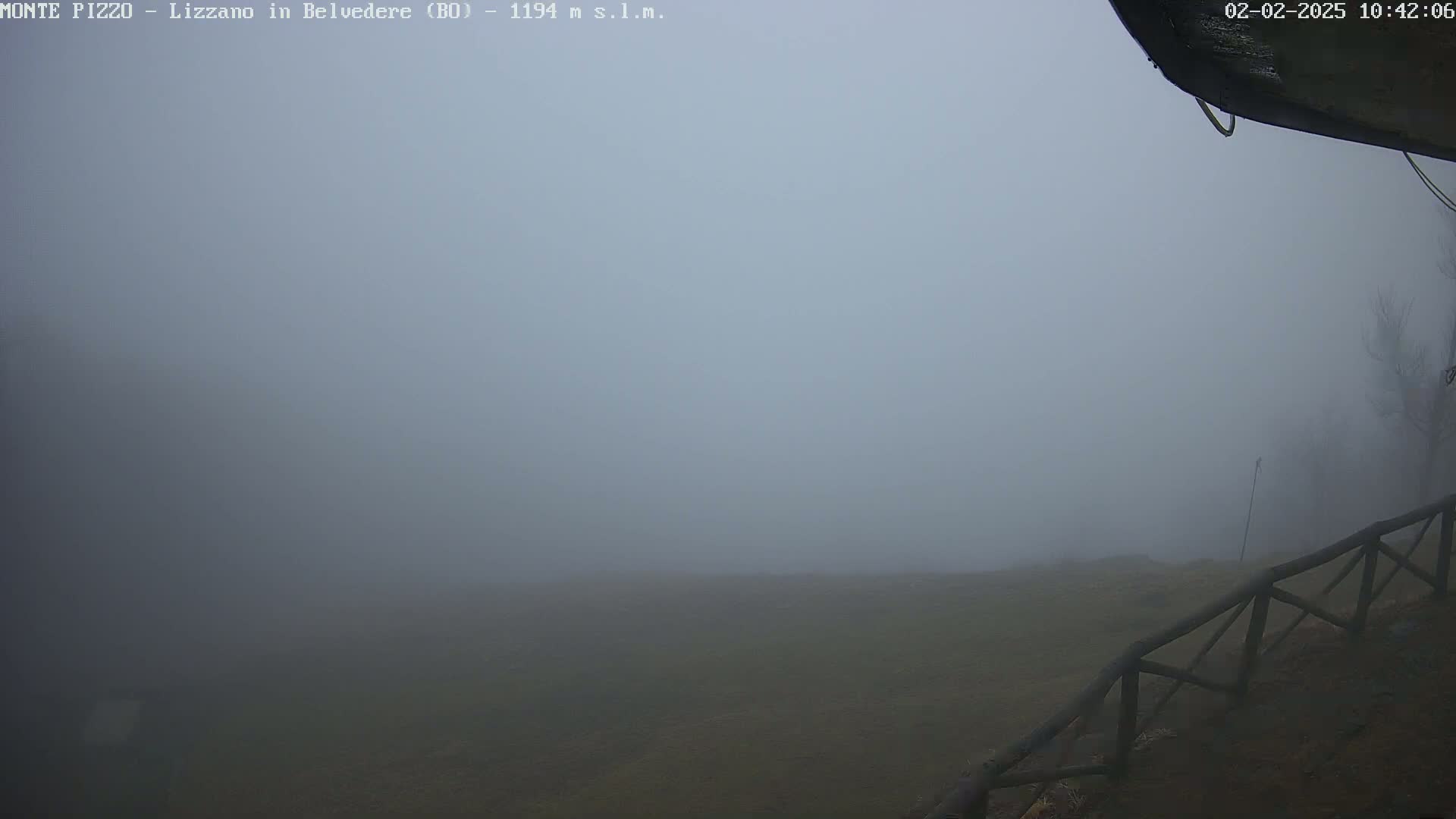 A thick fog obscures a view of a grassy field and a wooden fence.