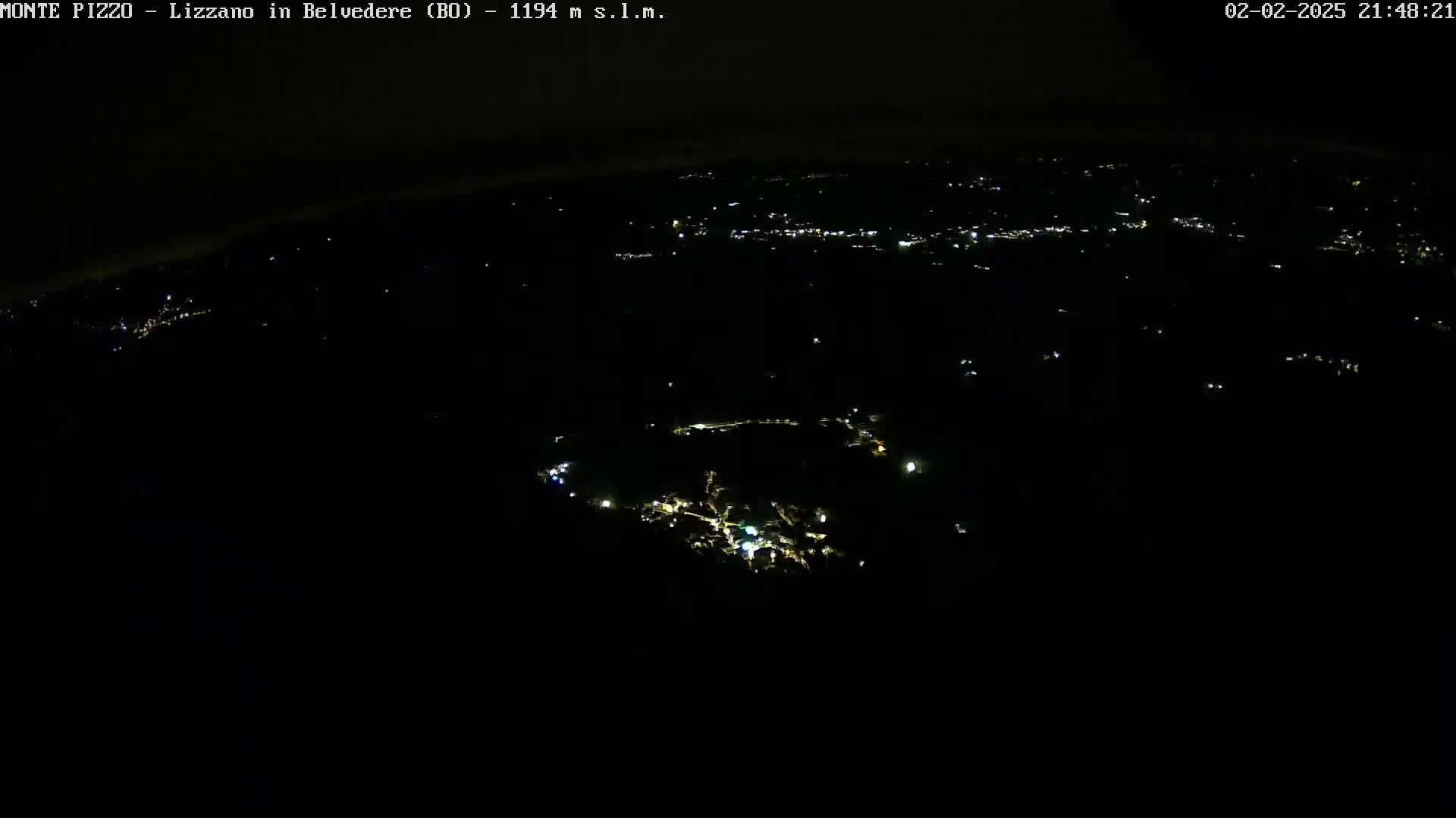 A nighttime, high-angle view shows a dark landscape speckled with small, scattered lights from a town or village below.