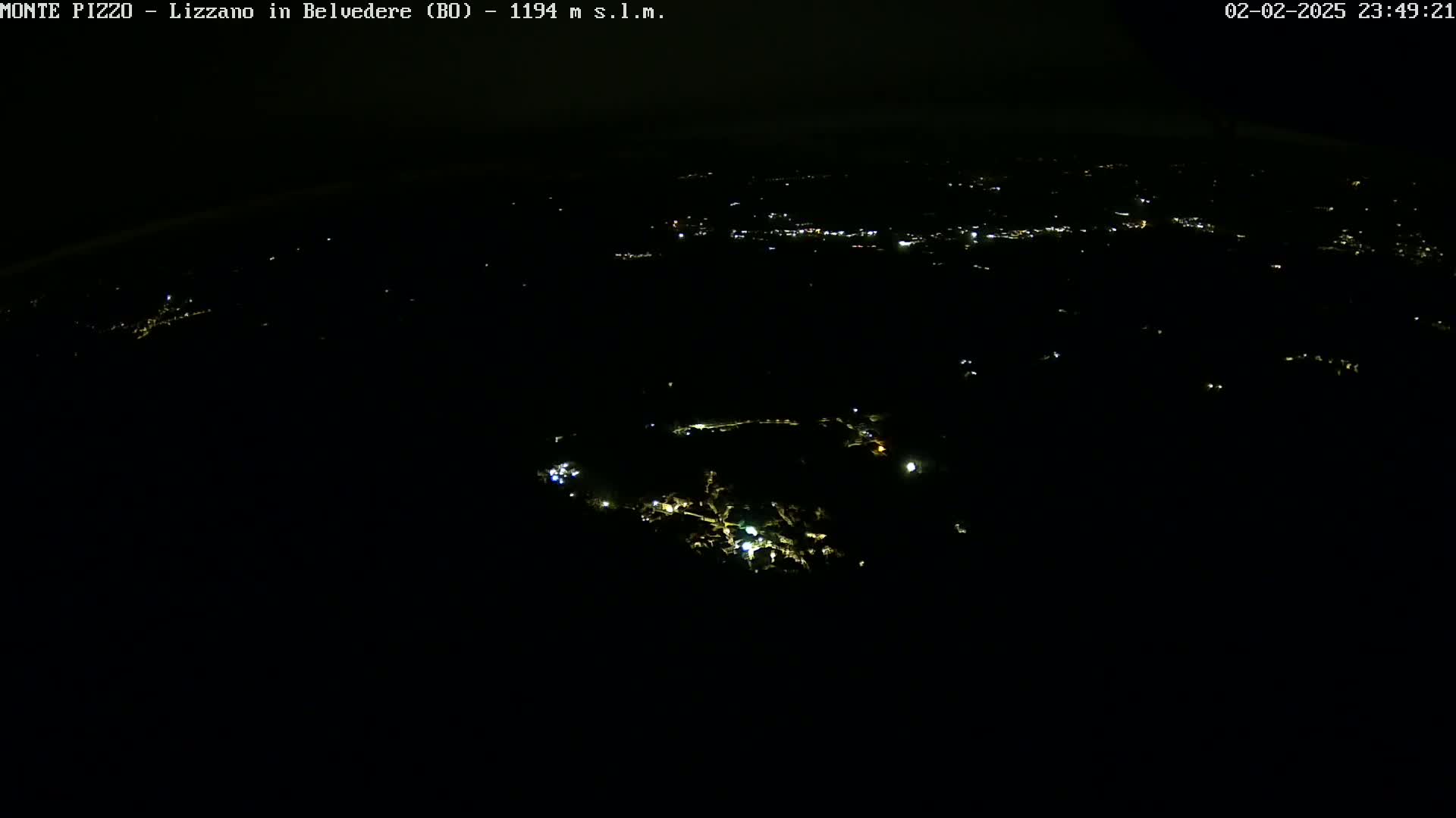 A nighttime, high-angle view shows sparsely scattered lights of a town or village below, under a dark sky.