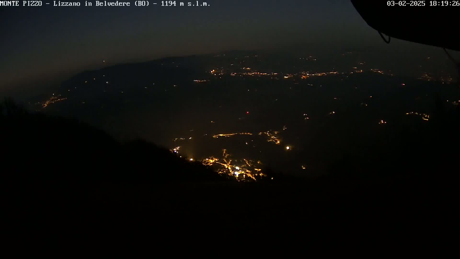 A nighttime, hazy view shows scattered lights from a valley below, illuminated against a dark sky.