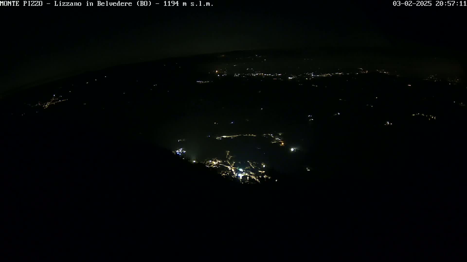 A nighttime, high-angle view shows a dark landscape speckled with faint, scattered lights from a town below.