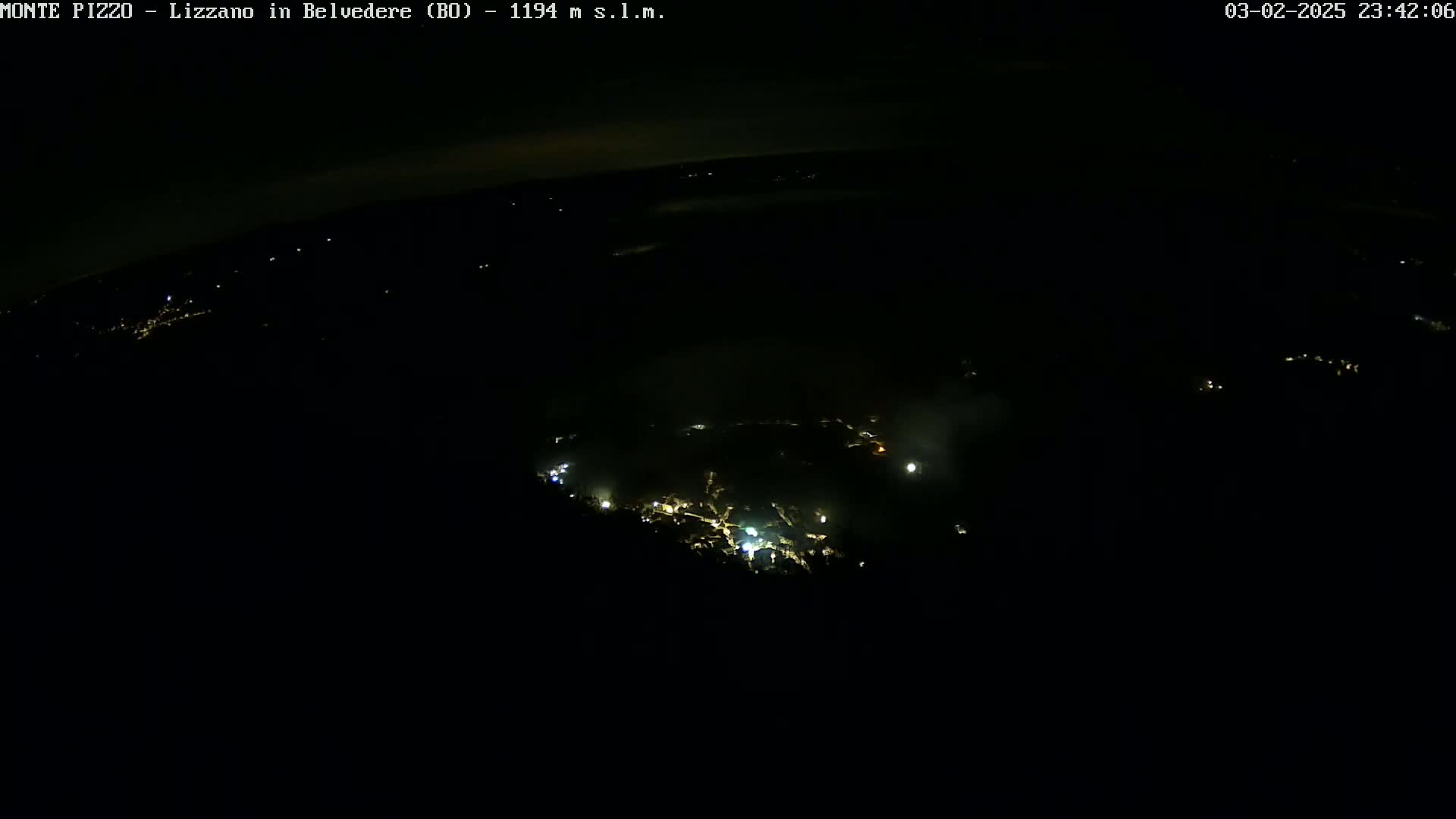 A nighttime aerial view shows a small town's scattered lights below, partially obscured by darkness and what appears to be fog or mist.