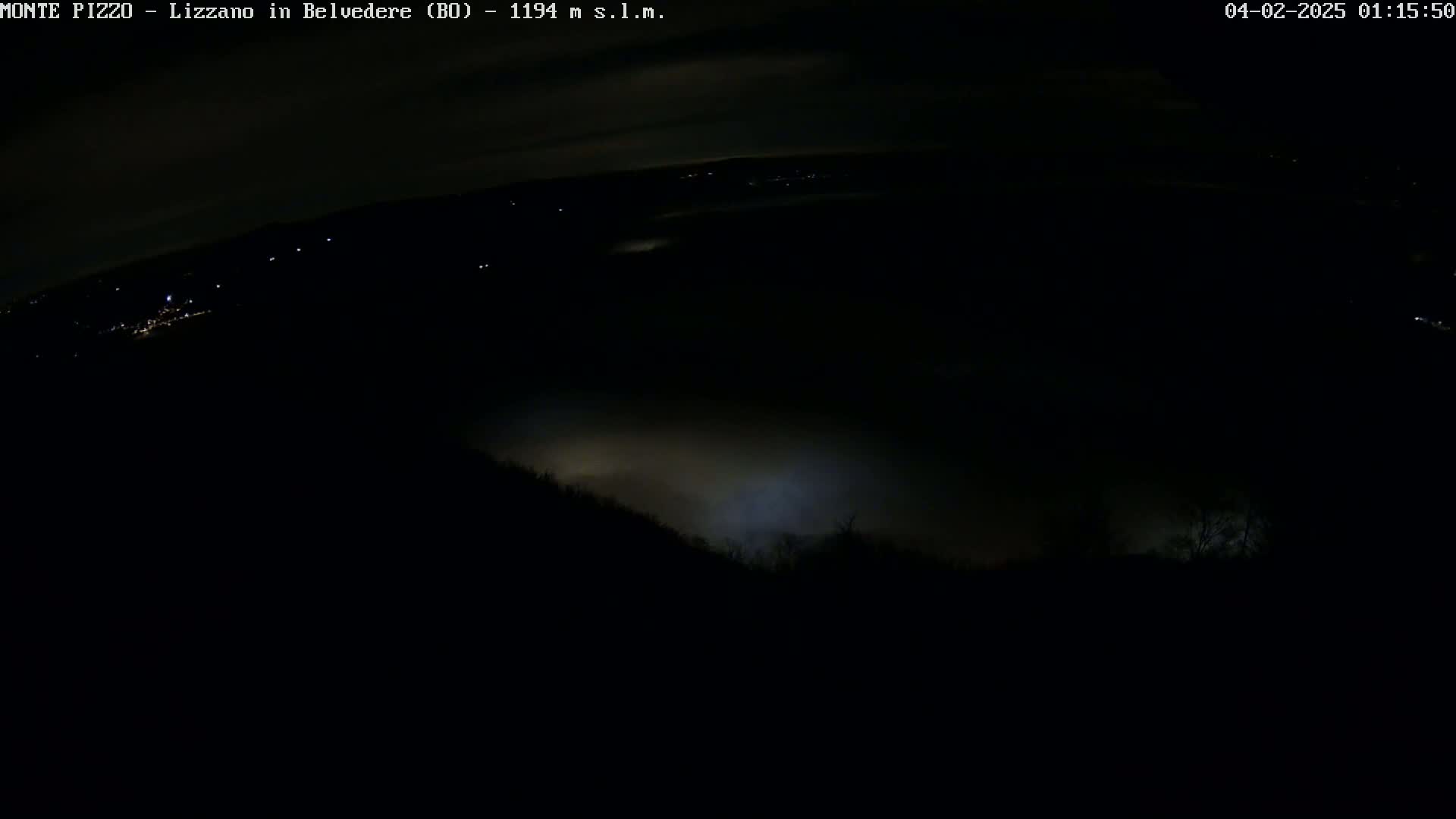 A nighttime, foggy view shows a dark landscape with a few distant lights and a low-lying fog obscuring the lower portion of the scene.