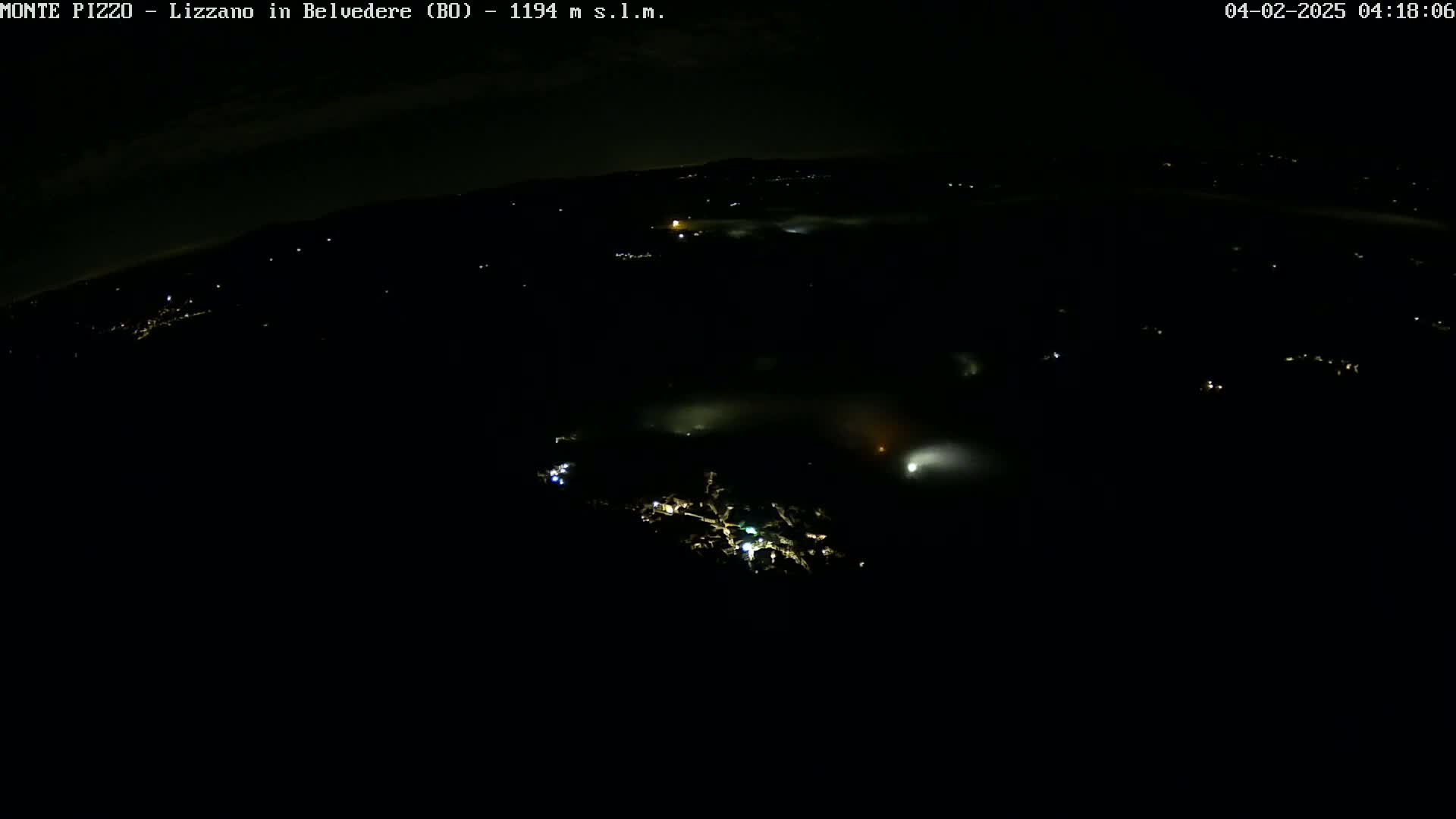 A nighttime, high-angle view shows a valley filled with low-lying fog and sparsely scattered lights.