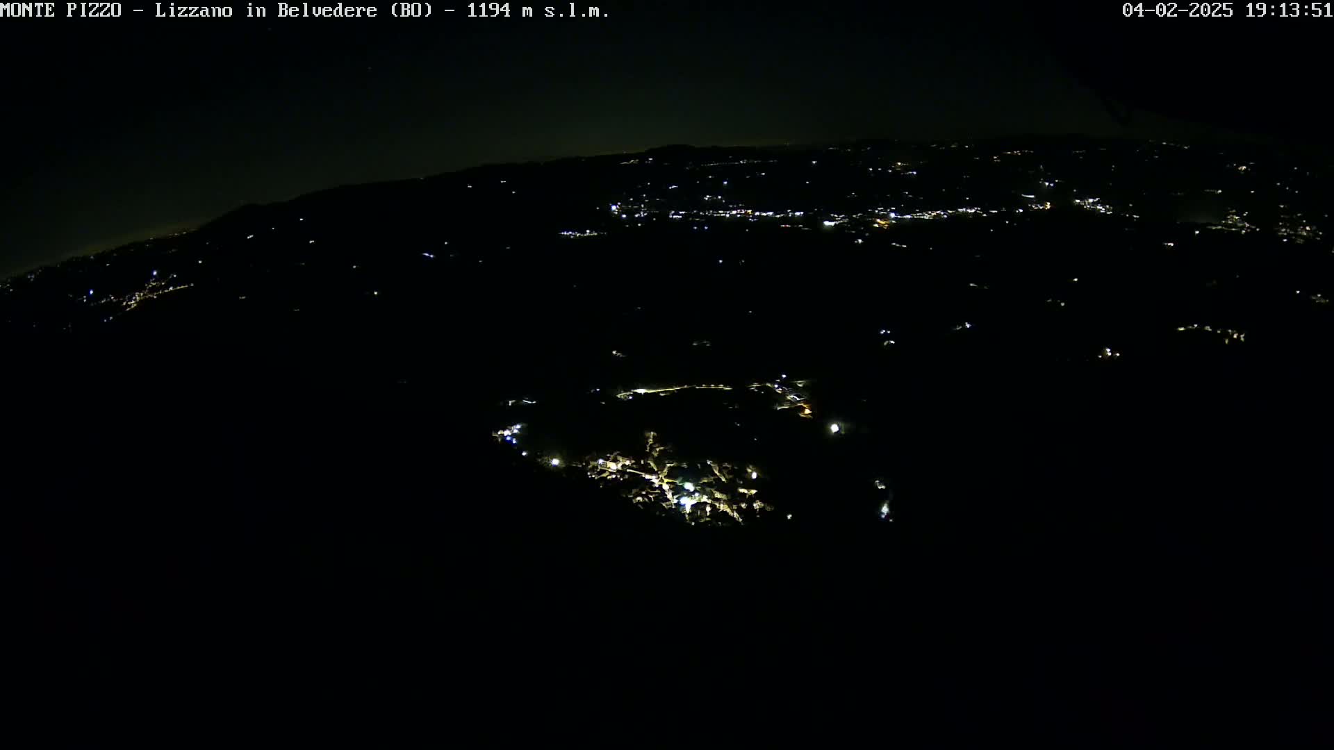 A nighttime aerial view shows a dark landscape with scattered lights from a town below.