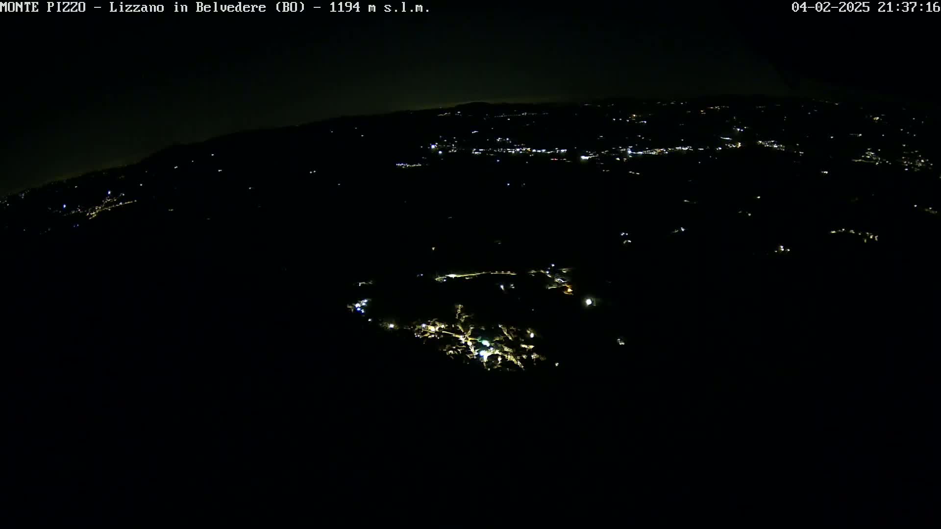 A nighttime, high-angle view shows a dark landscape speckled with small, scattered lights from a town or village below.