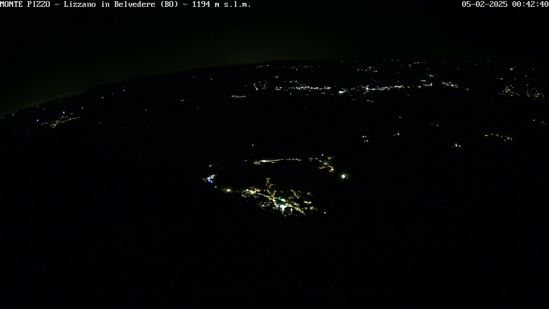 A nighttime, high-angle view shows a dark landscape speckled with faint, scattered lights from a town below.