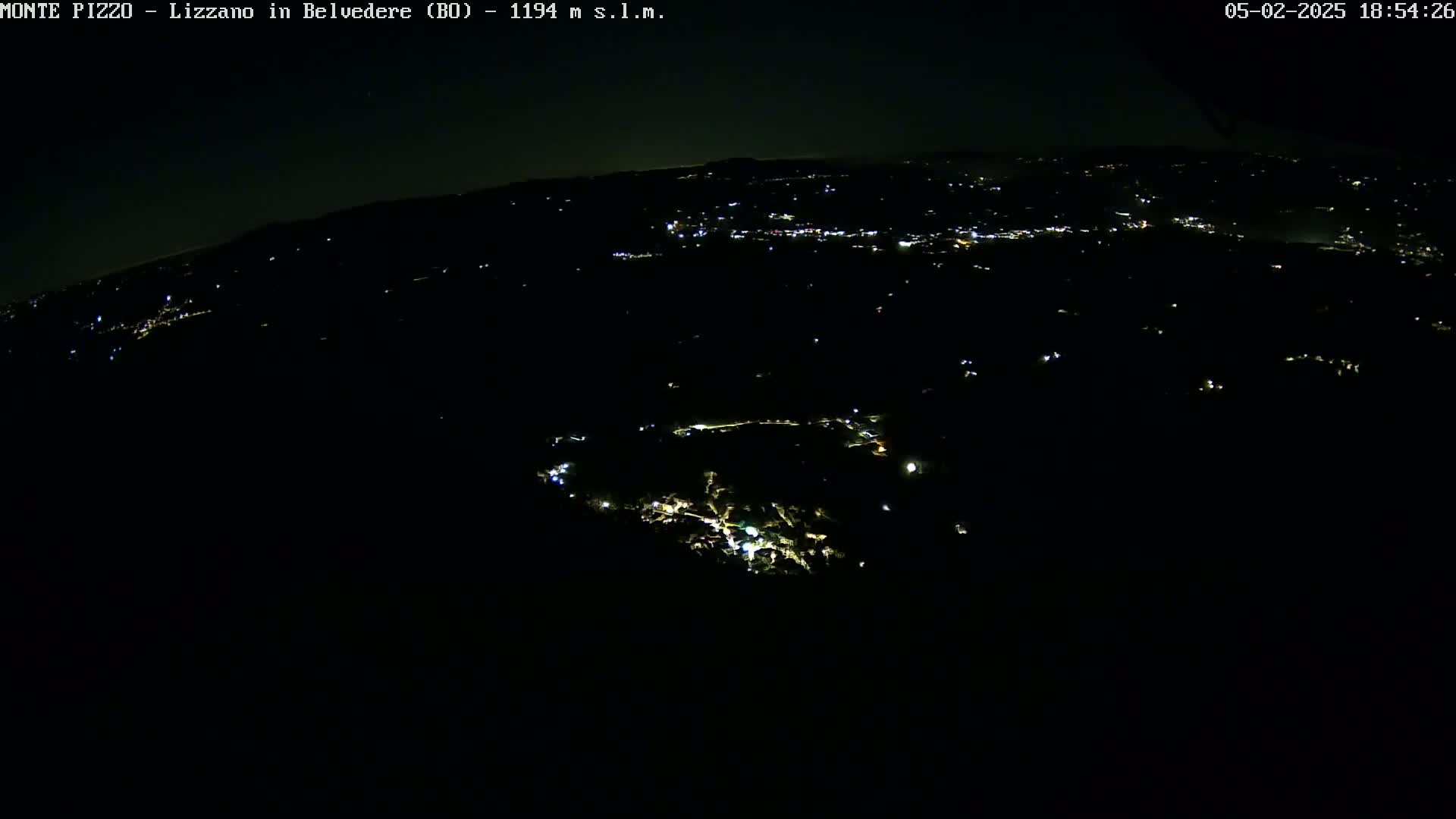 A nighttime aerial view shows a dark landscape sparsely dotted with the lights of a town or village under a clear, dark sky.