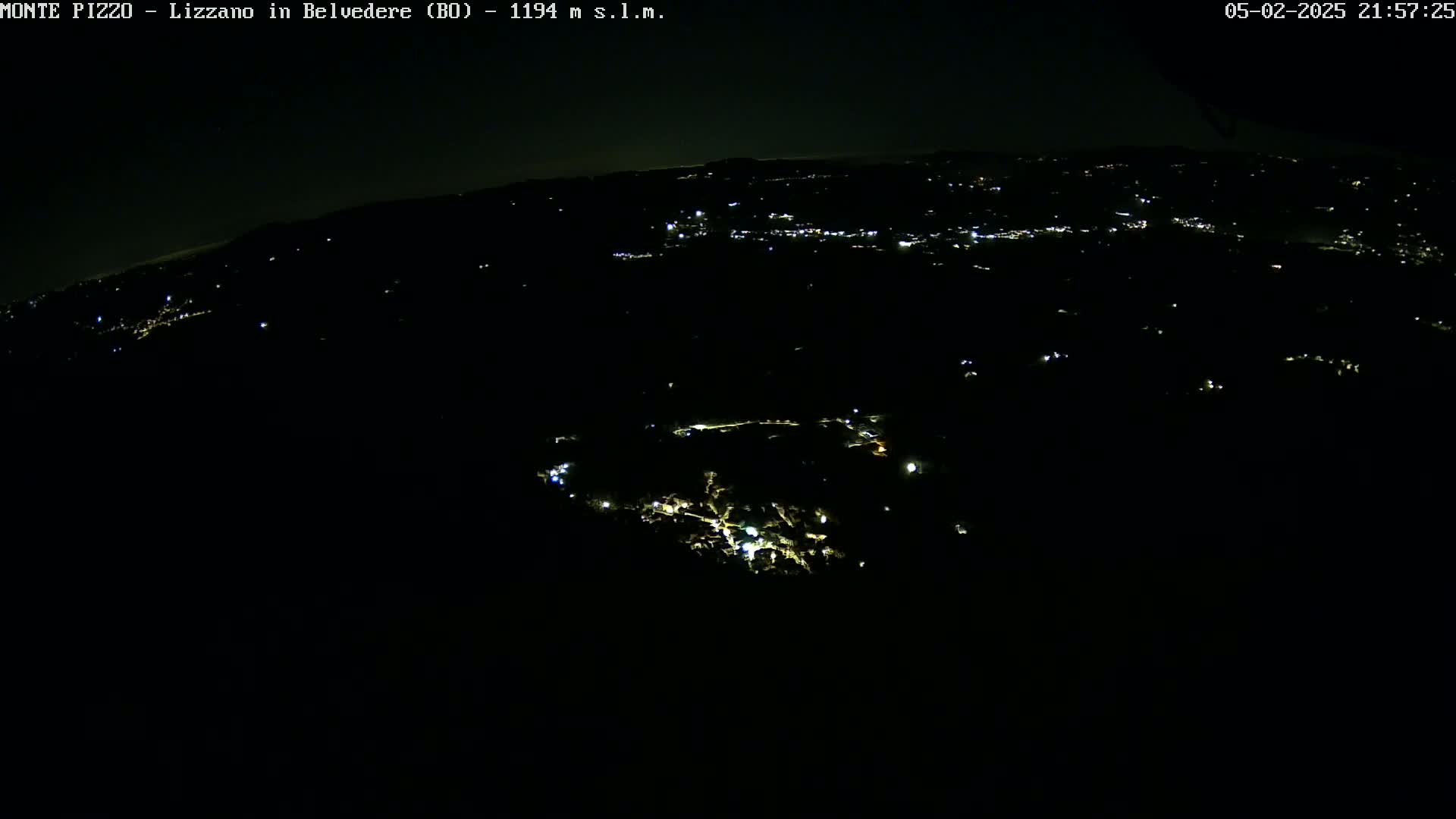 A nighttime, high-angle view shows a dark landscape sparsely dotted with the faint lights of a town or village.