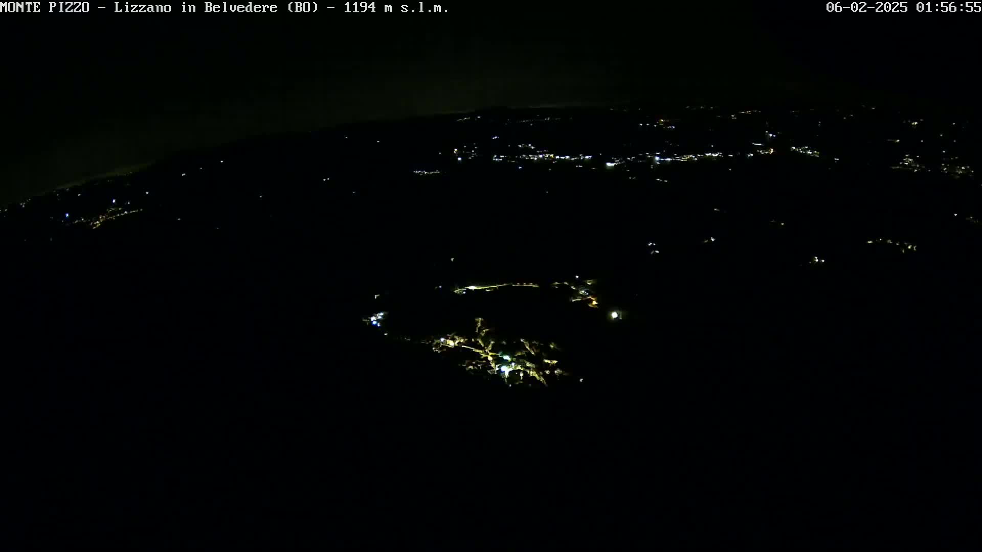 A nighttime, high-angle view shows a dark landscape with scattered, faint lights of a town or village below.
