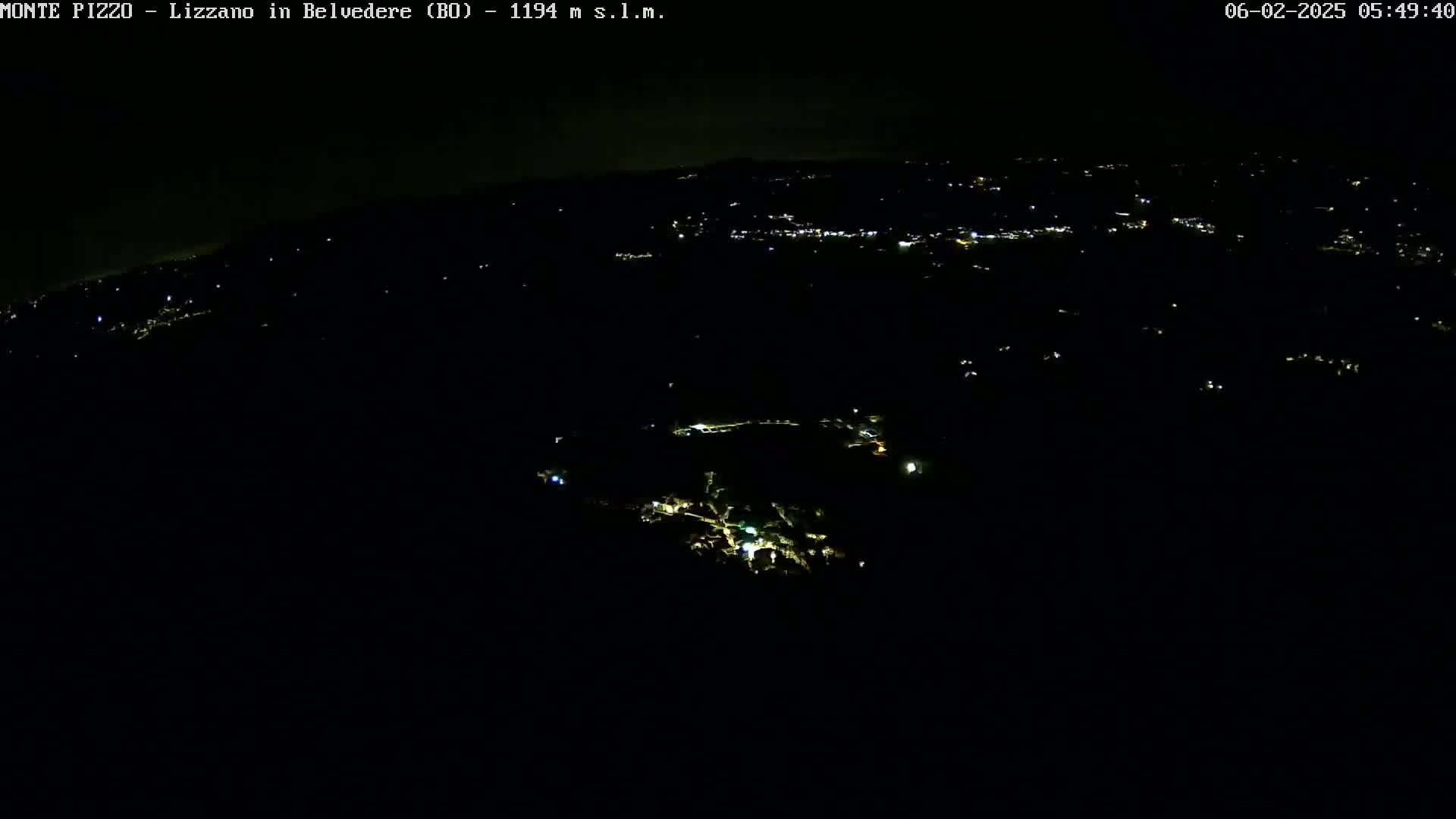 A nighttime aerial view shows a sparsely lit landscape with a few clusters of lights possibly indicating towns or villages.