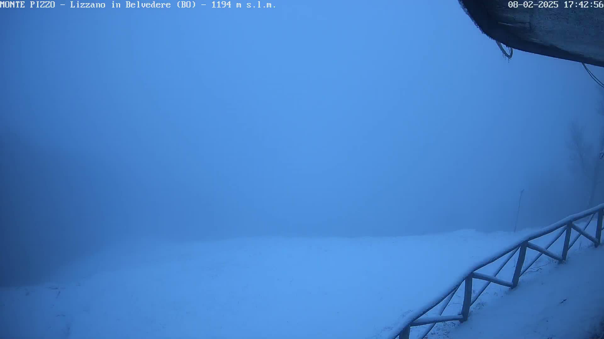 A snow-covered landscape is visible through a thick fog, with a wooden fence in the foreground.