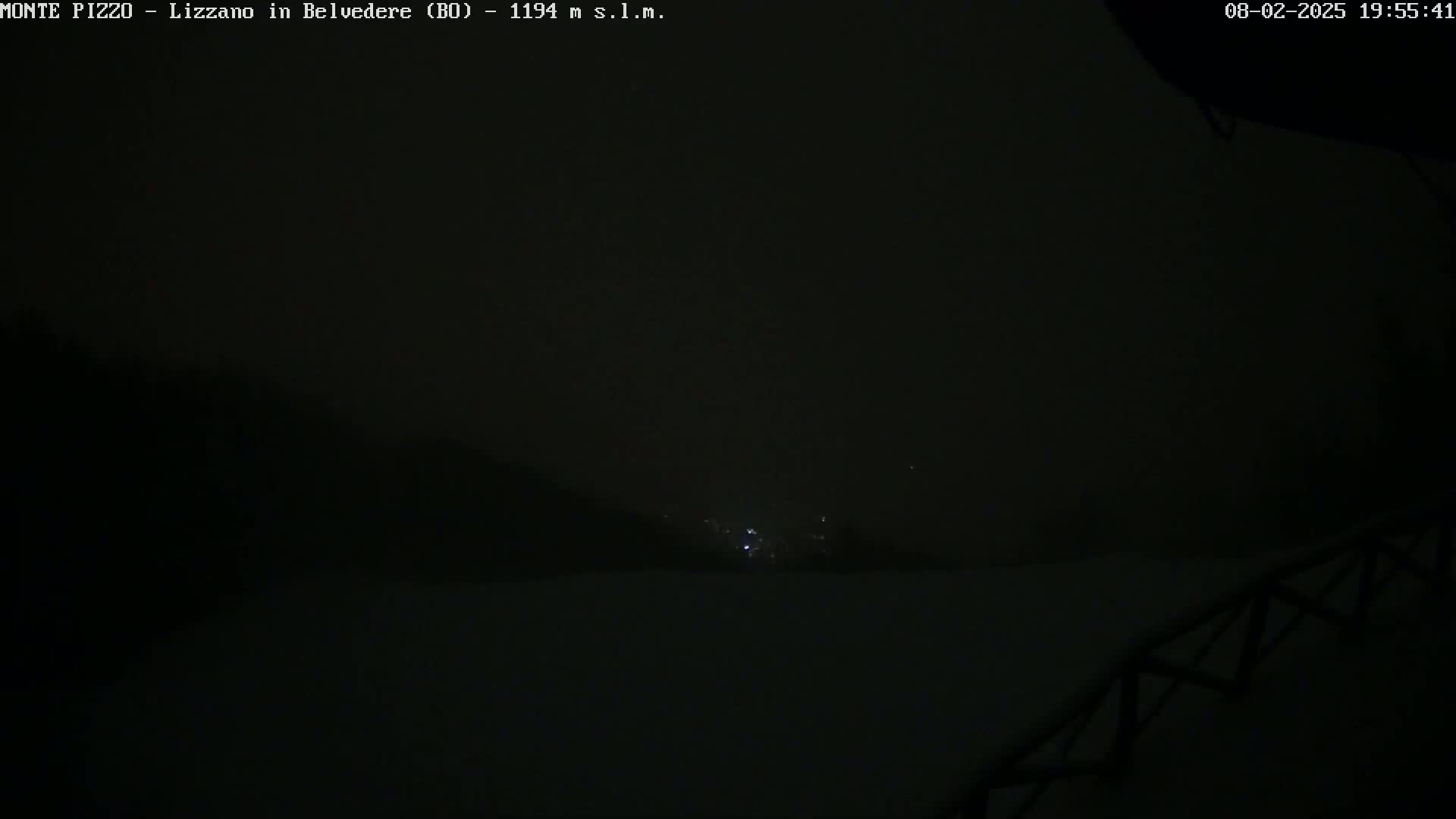 A nighttime, dark and foggy view shows a few faint lights in the distance.