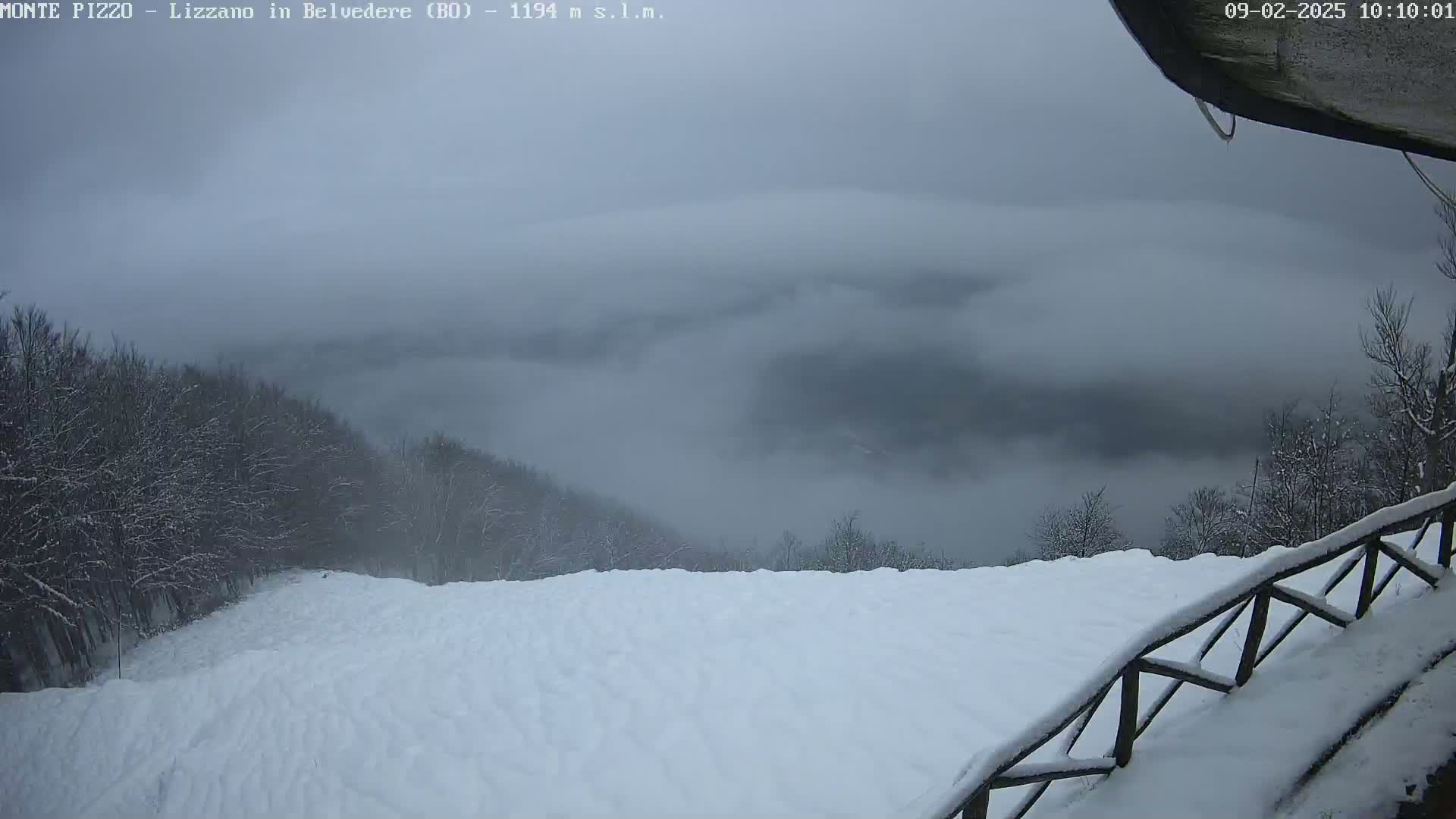 A snow-covered hillside and a foggy valley are visible from a snowy viewpoint, under an overcast sky.