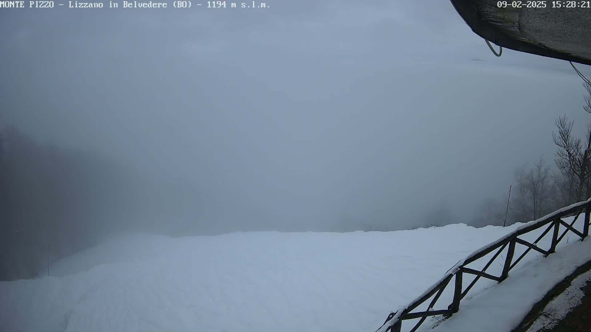 A snowy, foggy landscape is visible from a high vantage point, with a wooden fence partially in the foreground.