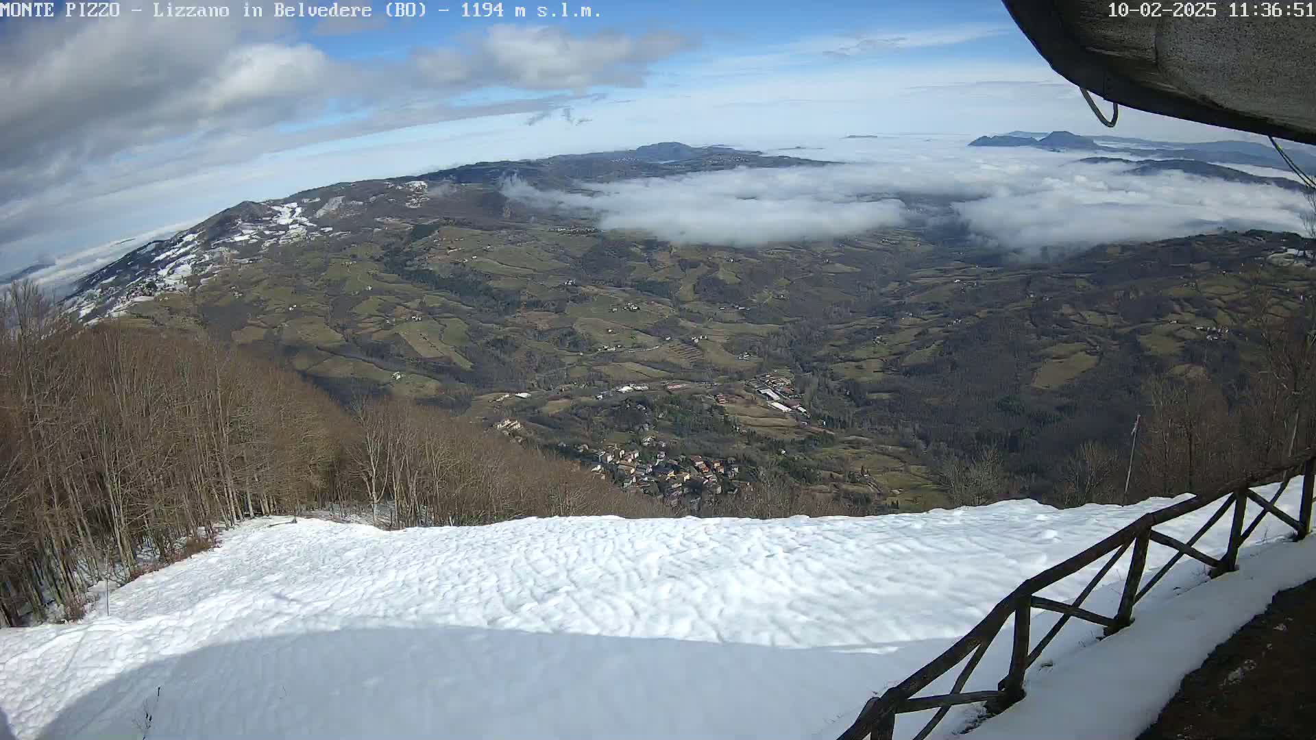 A snowy hillside overlooks a valley covered in low clouds under a partly sunny sky.