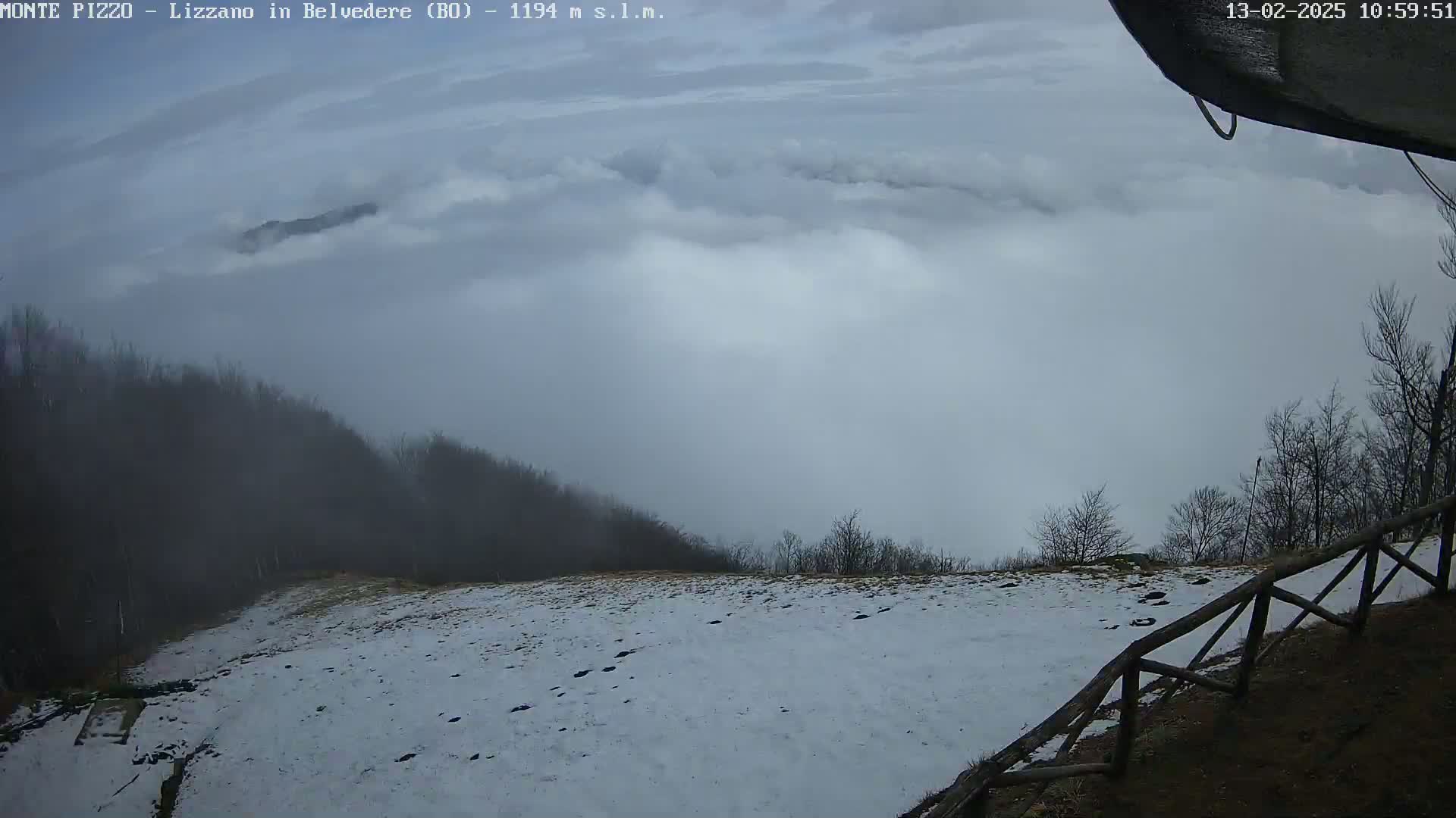 A snow-covered hillside overlooking a valley filled with low-lying clouds under an overcast sky.