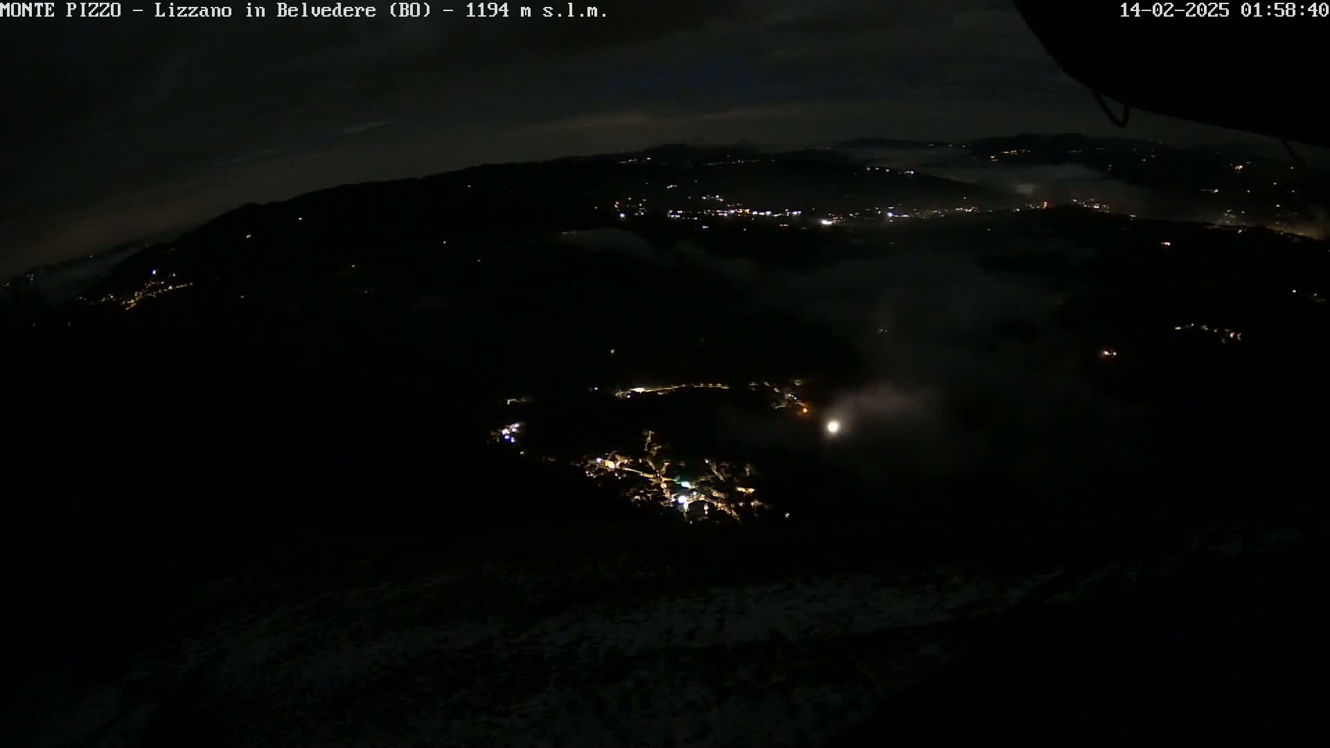 A nighttime, high-angle view of a valley shrouded in fog with scattered lights from a town visible below.
