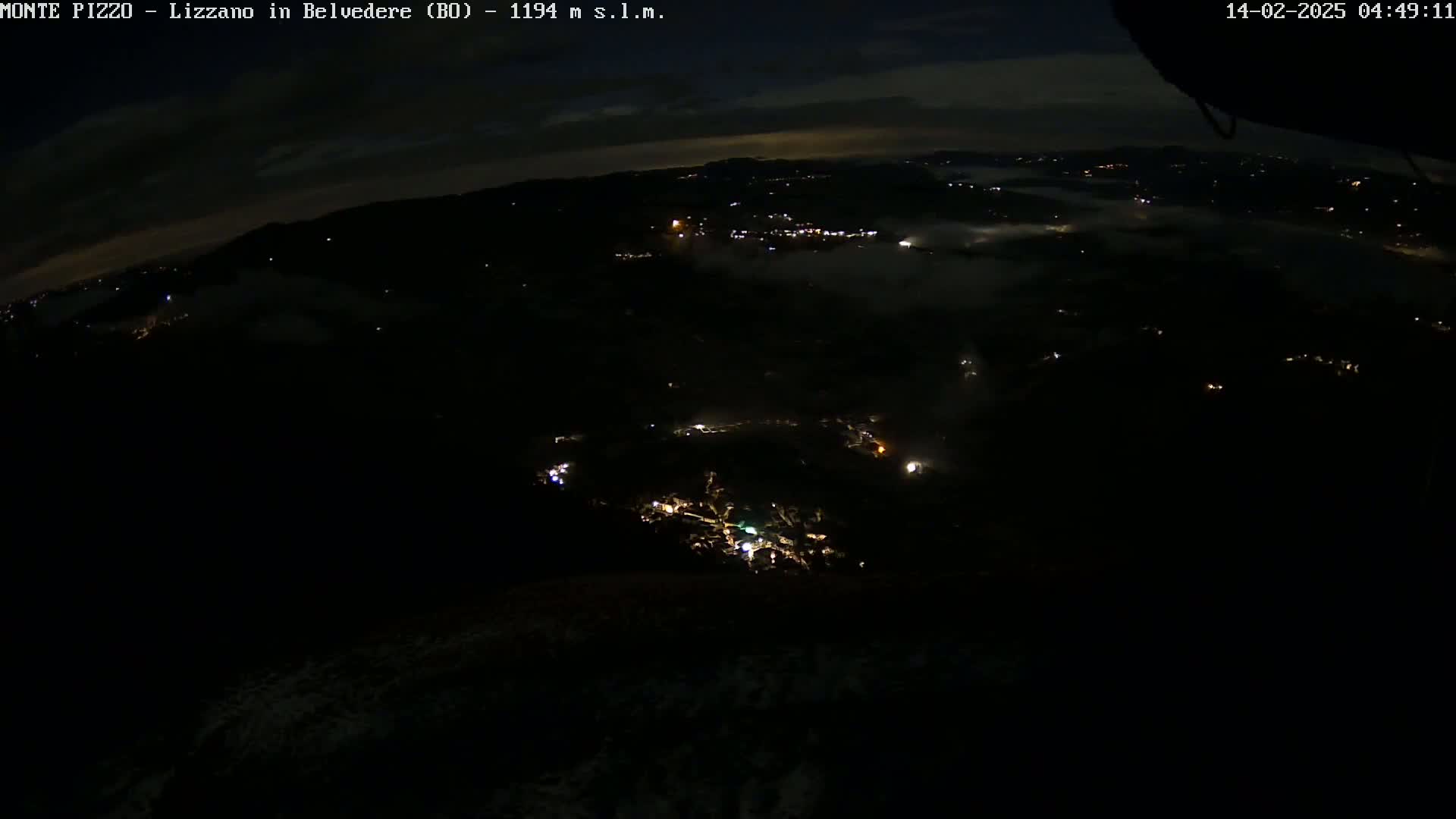A nighttime aerial view shows a valley partially covered in fog with scattered lights from a town below.