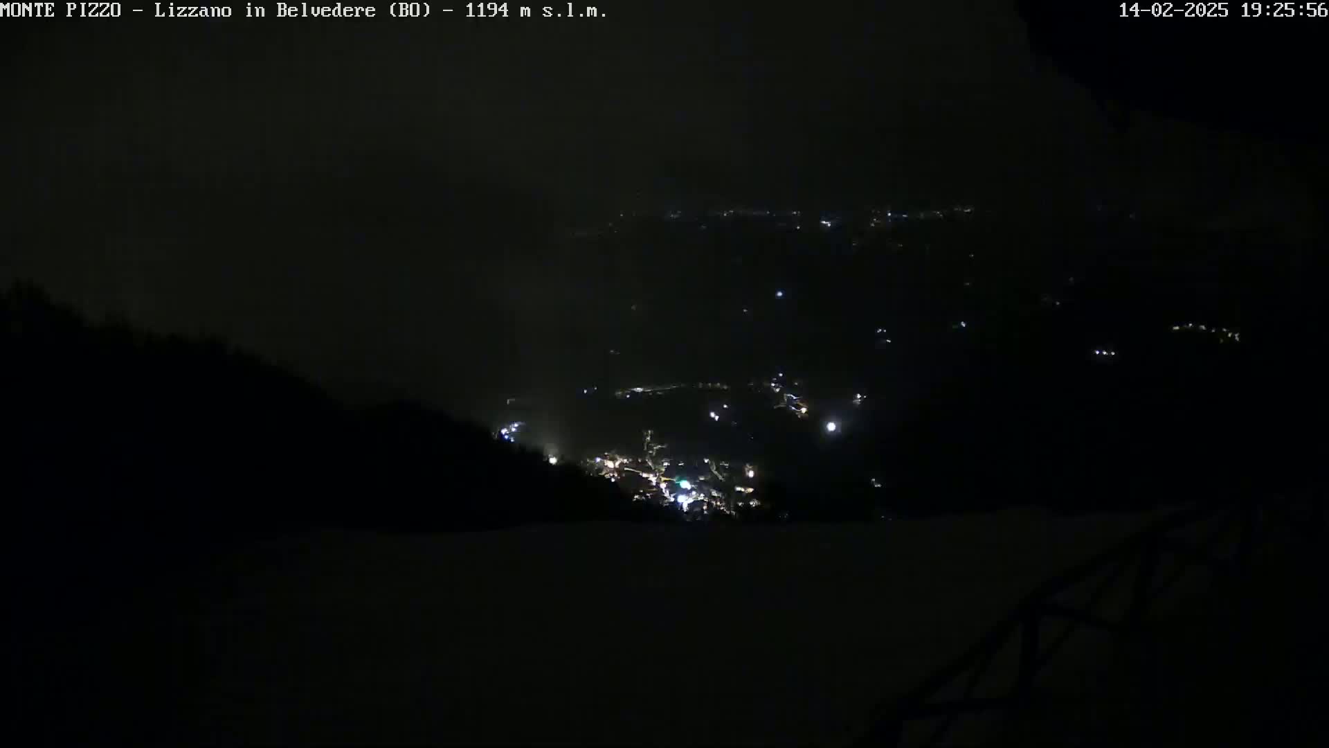 A nighttime view from a high vantage point shows a valley with scattered lights below, under a dark, possibly cloudy sky.