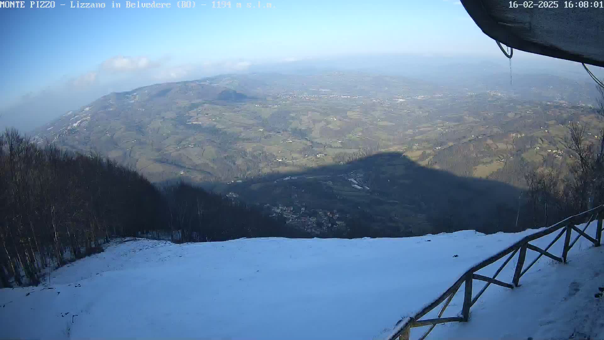A snow-covered mountaintop overlooks a vast valley under a clear, sunny sky.